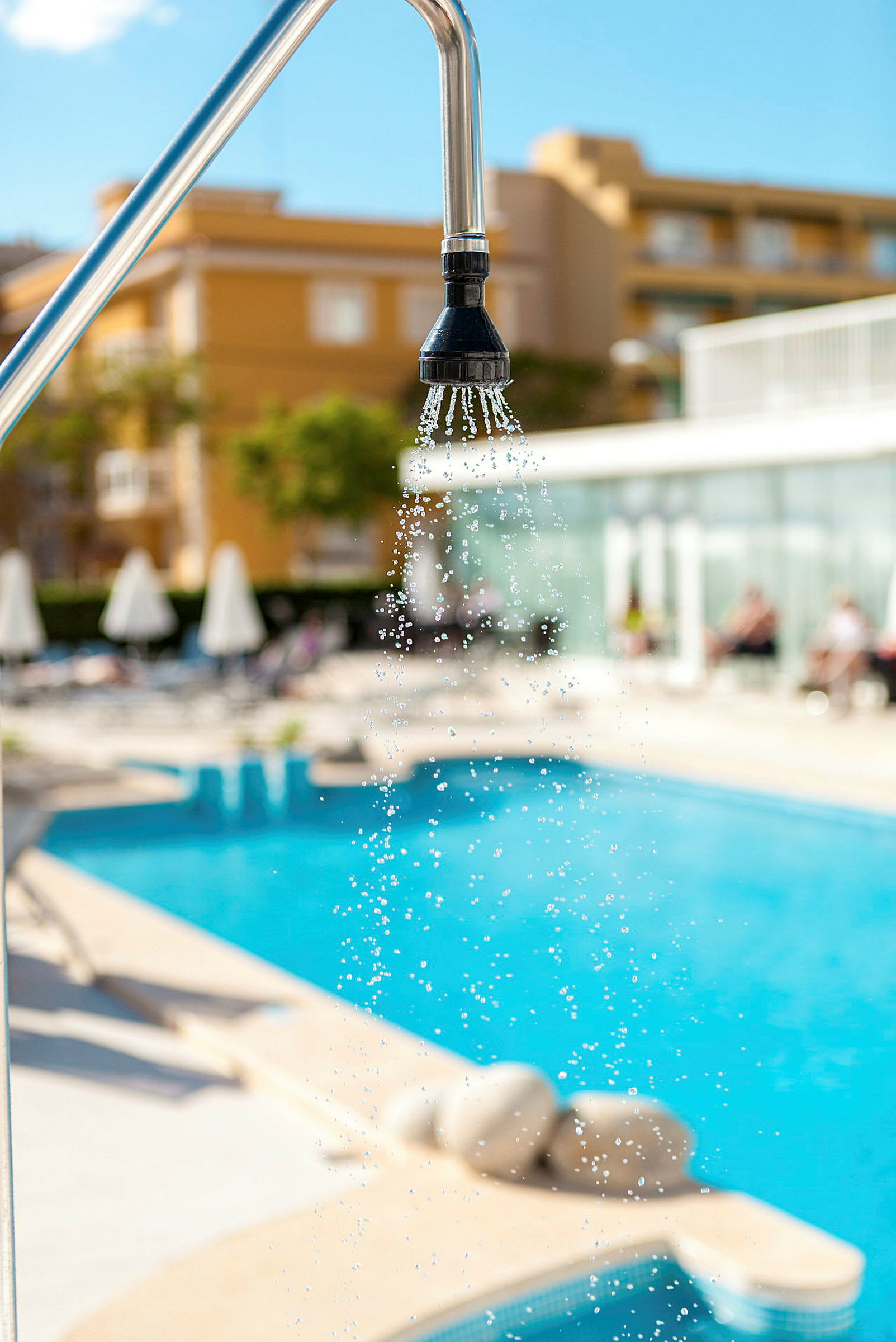 Bruseren ved en swimmingpool, med parasoller og bygning i baggrunden. (AI-genereret tekst)