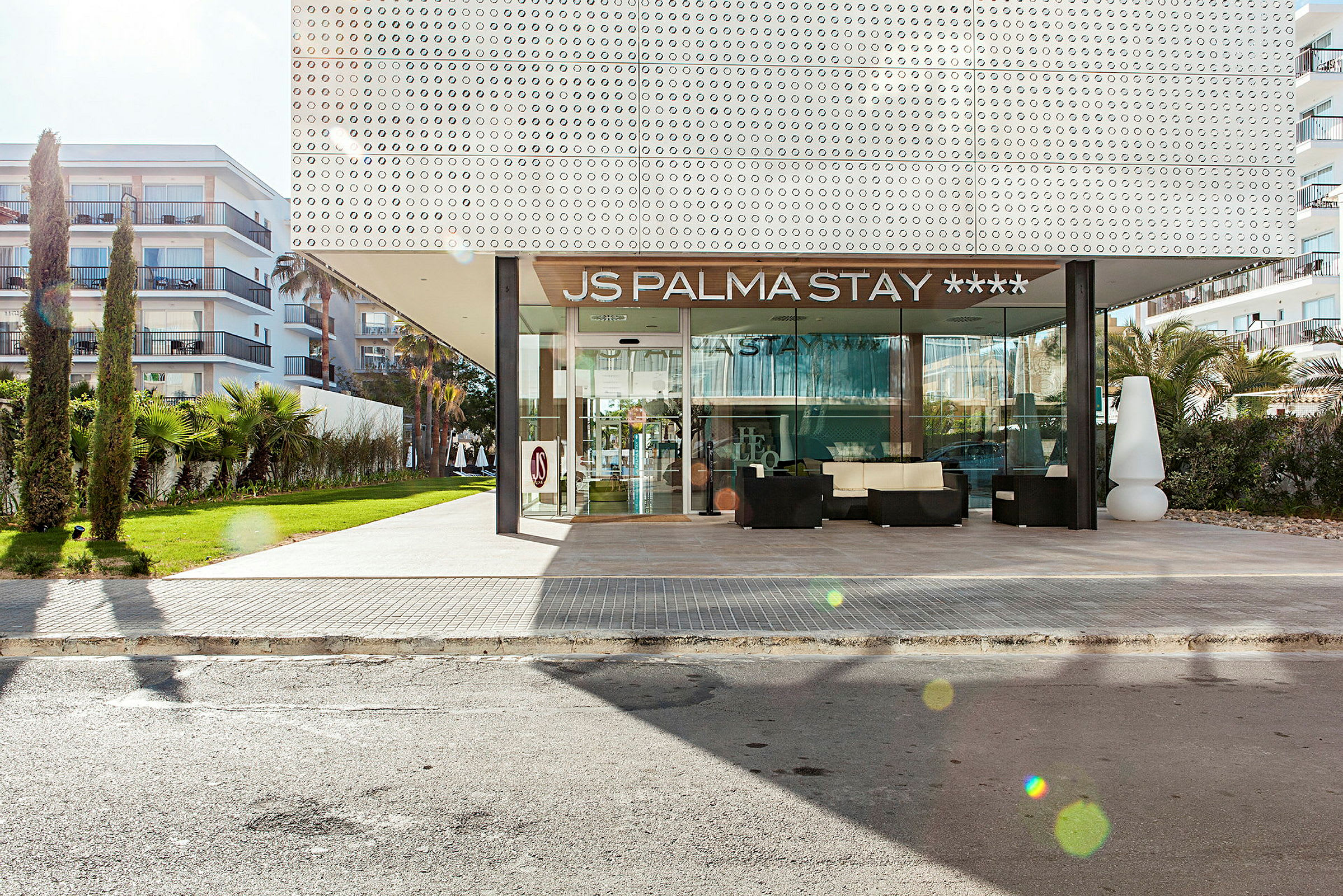 Udvendig af JS Palma Stay hotel med indgang og omkringliggende grønne områder. (AI-genereret tekst)