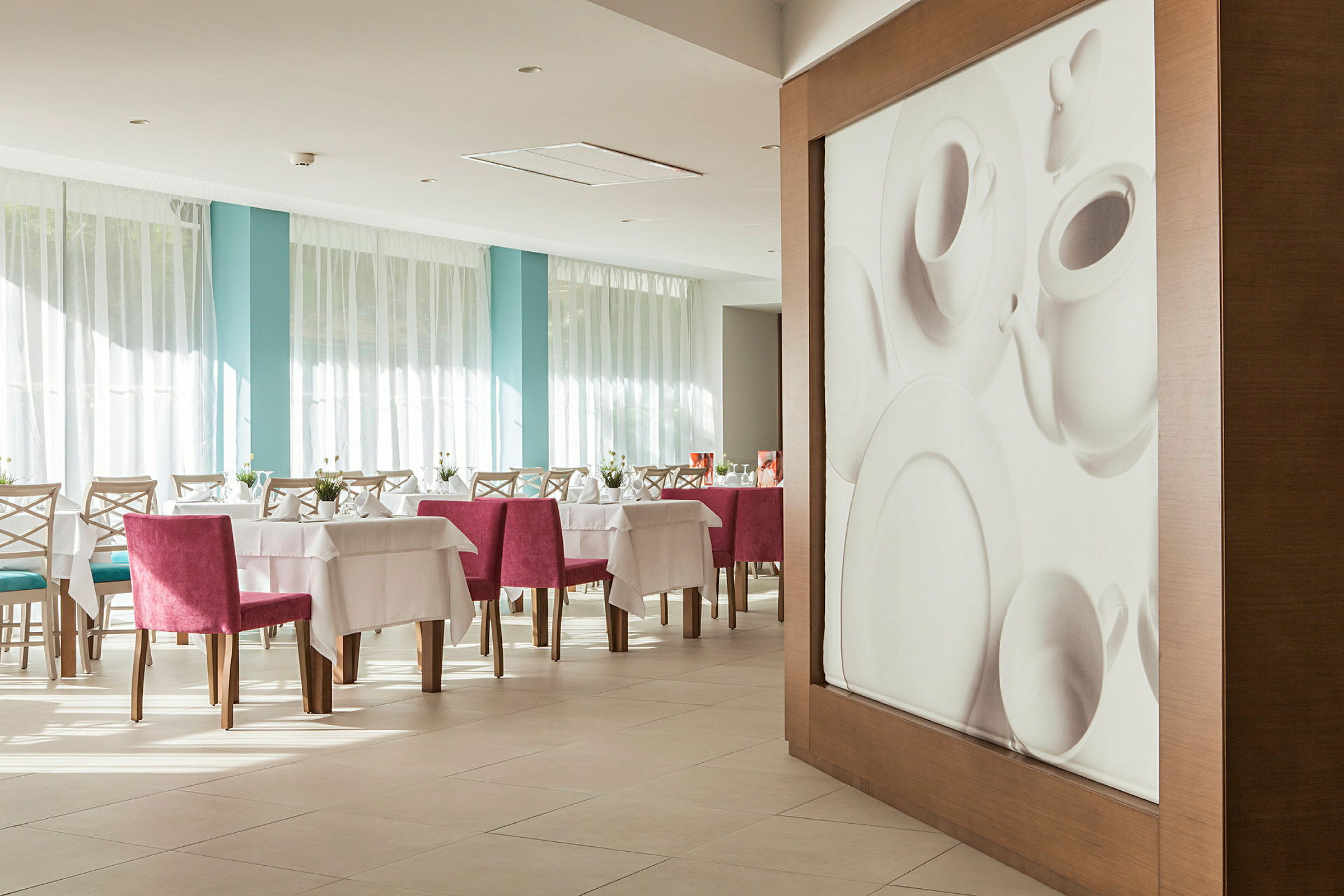 Interiør af en restaurant med dækkede borde og lyserøde stole samt en vægdekoration, der forestiller porcelæn. (AI-genereret tekst)