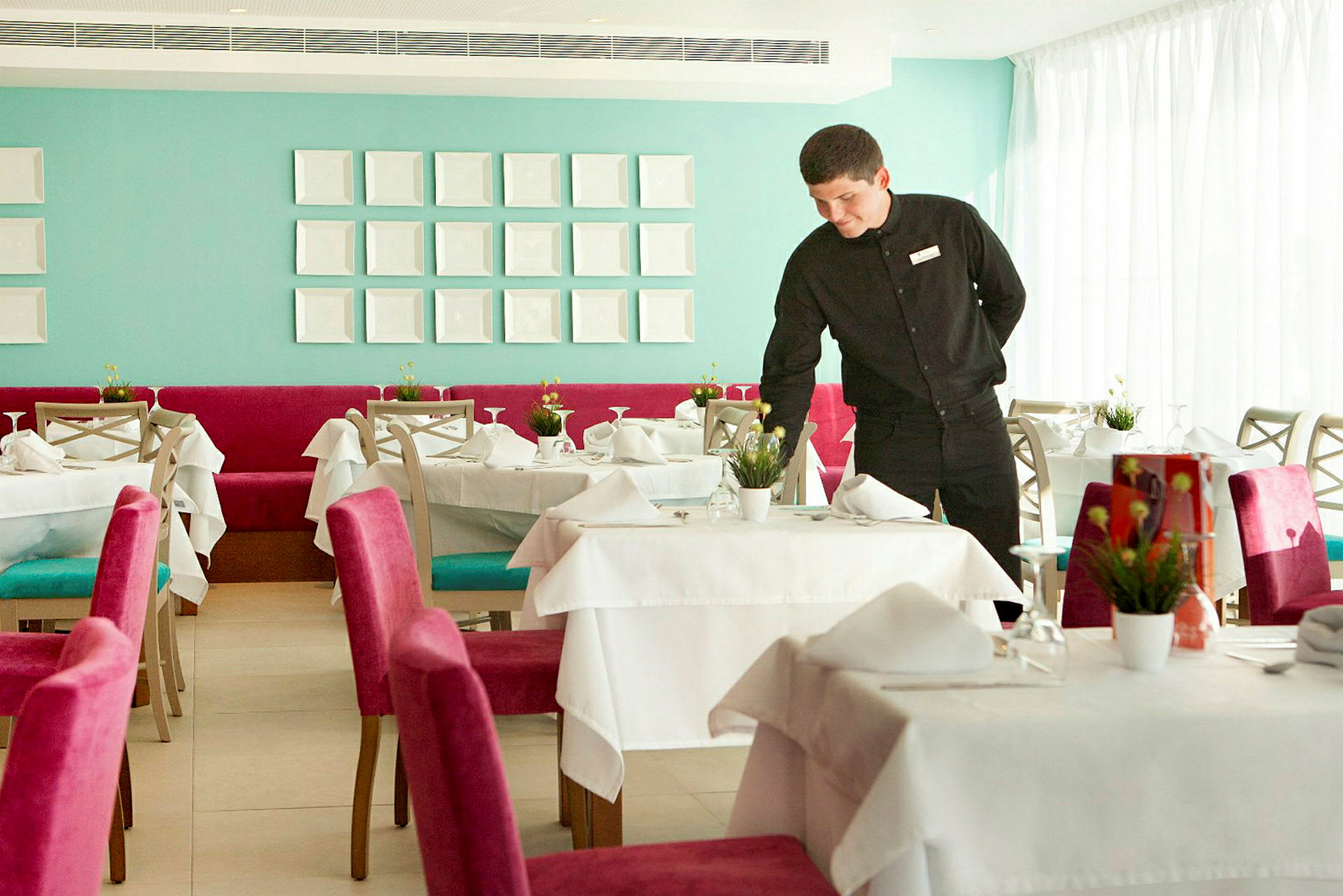 En elegant restaurant med dækkede borde og farverige stole, en servicemedarbejder gør et bord klart. (AI-genereret tekst)