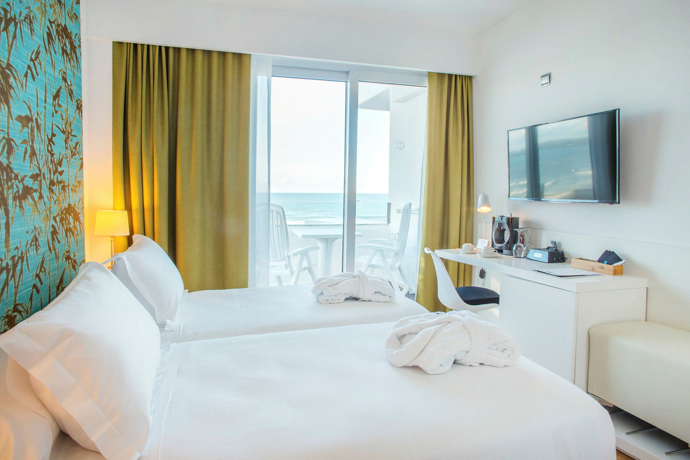Hotelværelse med to senge, skrivebord, væg-TV og havudsigt fra altanen. (AI-genereret tekst)