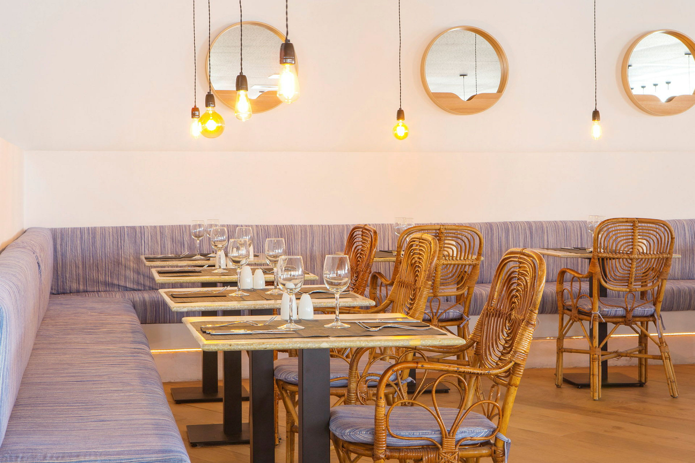 Restaurant med fletstole og borde, lyse hængende lamper og spejle på væggen. (AI-genereret tekst)