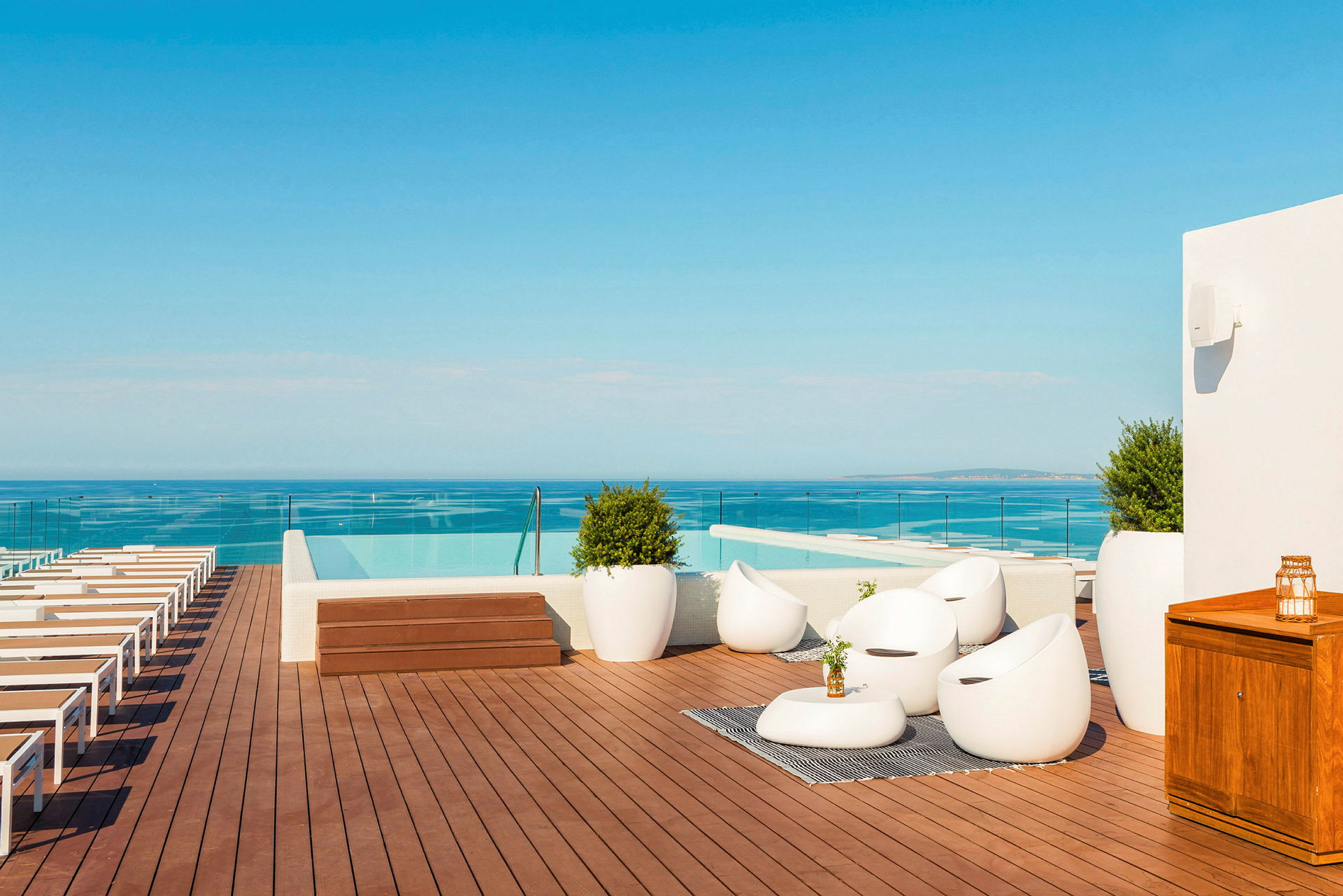 En tagterrasse med liggestole, siddeområde og infinitypool med udsigt over havet. (AI-genereret tekst)