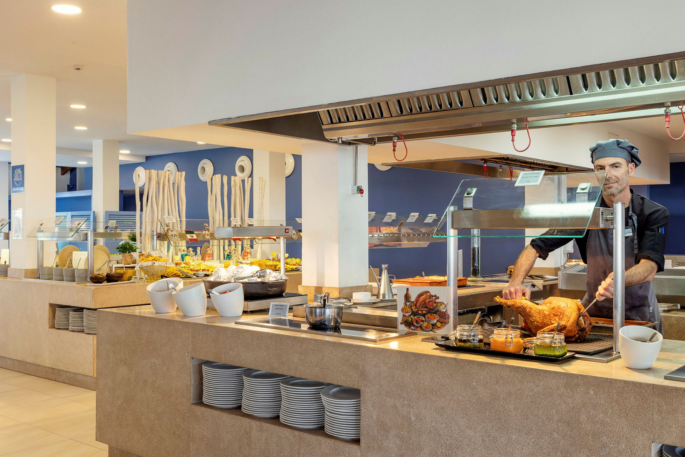 En kok står og skærer kød bag en disk med en salatbuffet i baggrunden. (AI-genereret tekst)