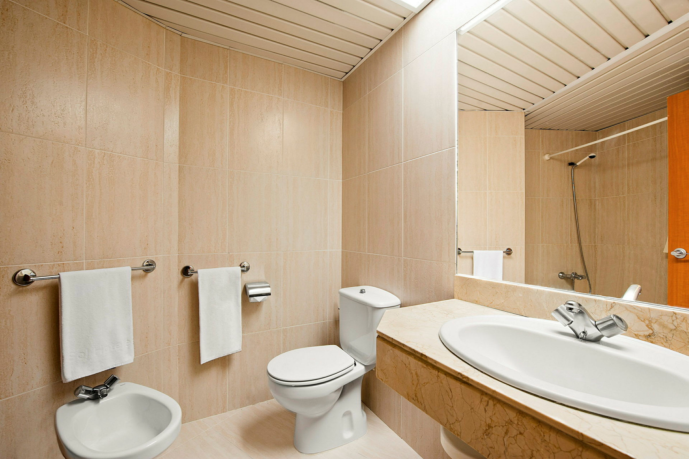 Et badeværelse med beige flisevægge, toilet, bidet og en håndvask med marmorbordplade. (AI-genereret tekst)
