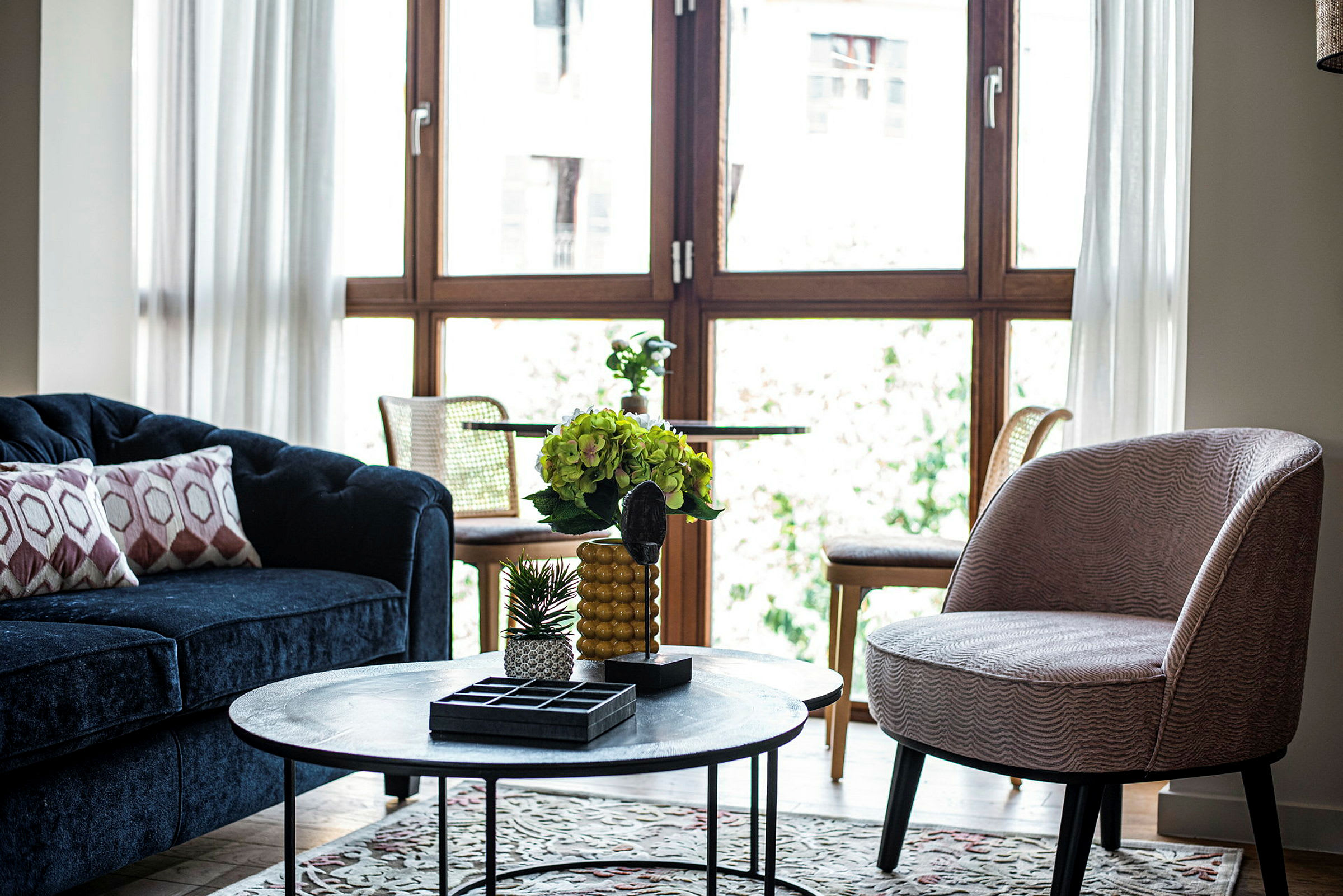 Stue med blå sofa, rund bordlampe og store vinduer. (AI-genereret tekst)
