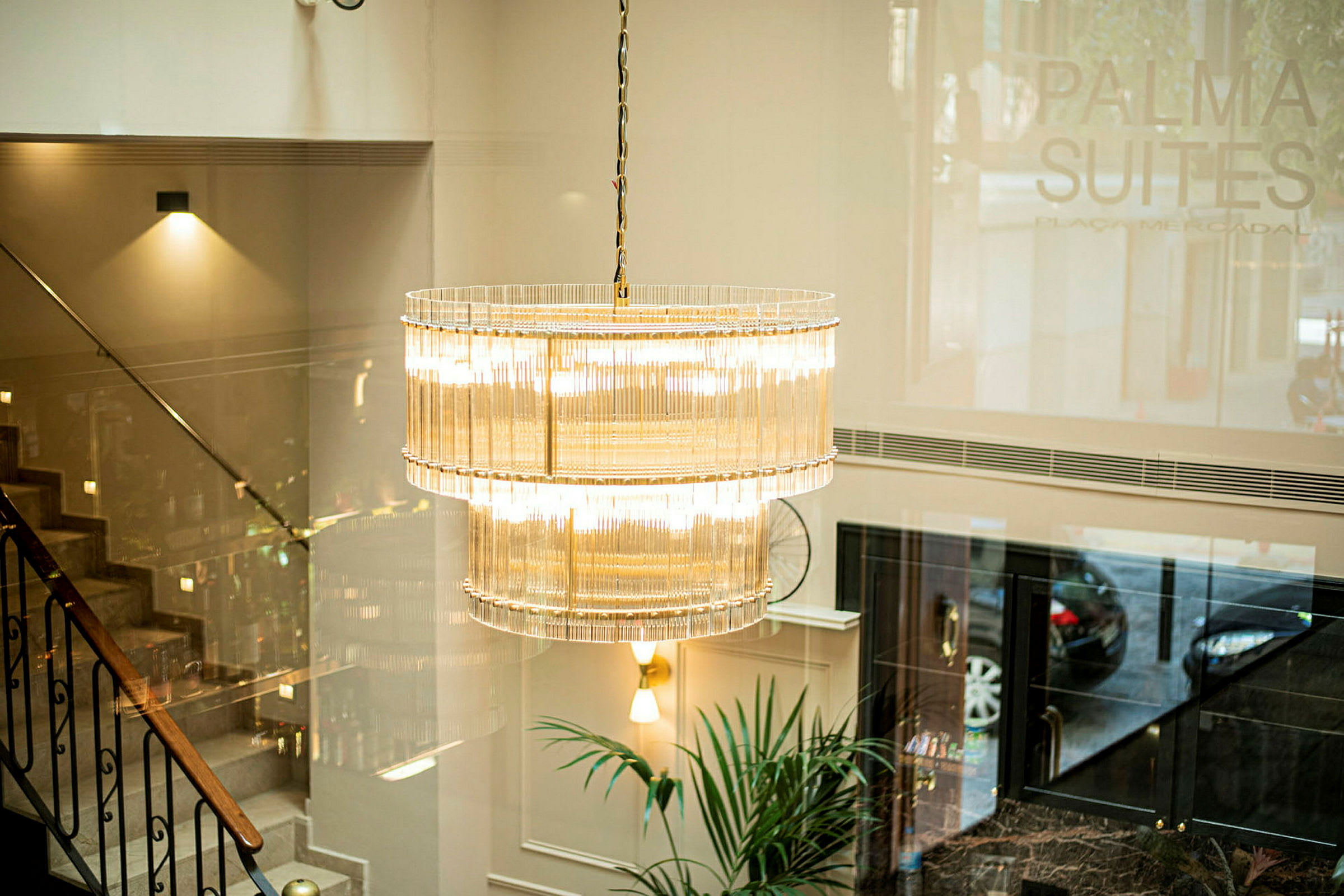 En elegant lysekrone hænger i en lobby med trappe og plante synligt. (AI-genereret tekst)