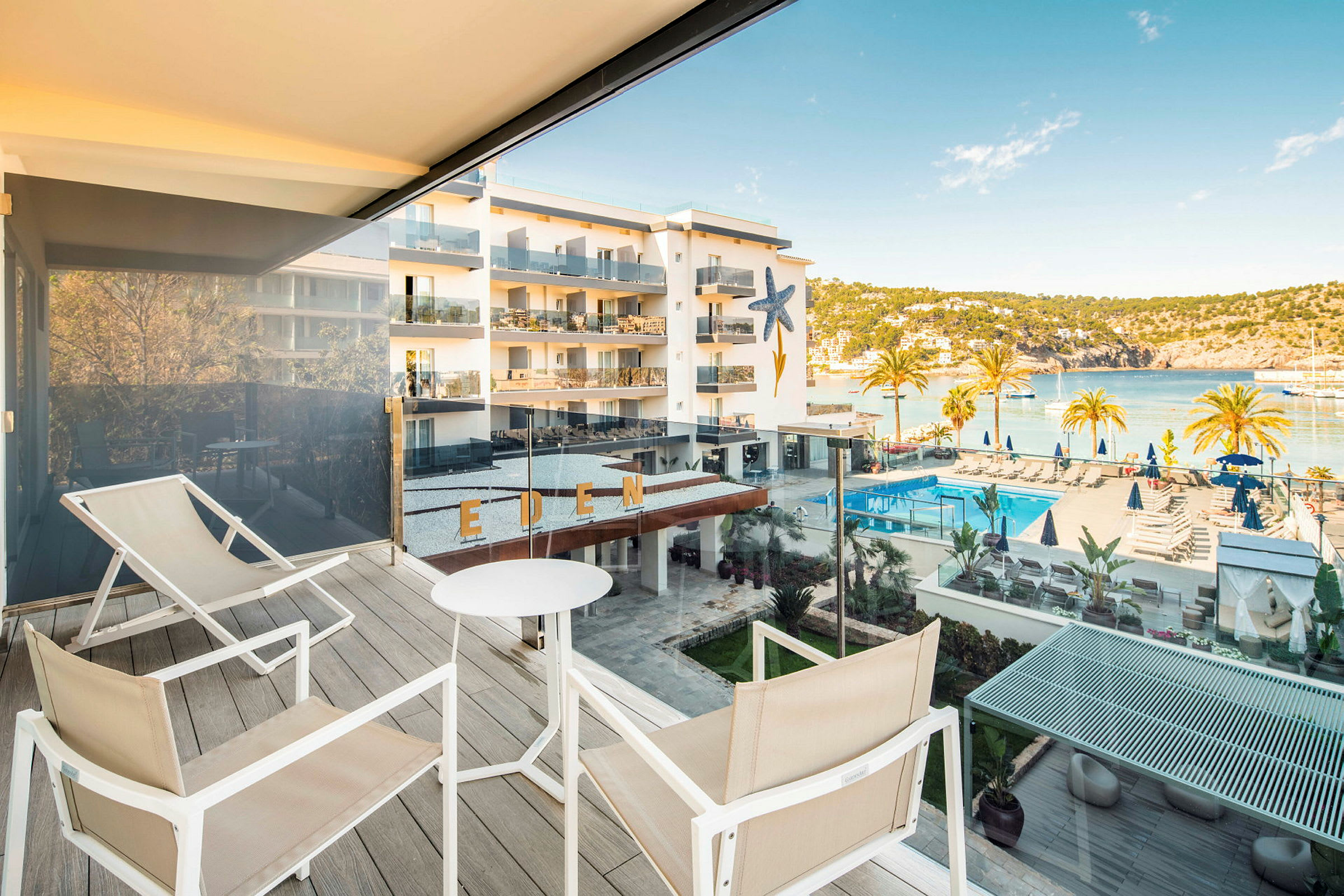 Udsigt fra en terrasse med siddepladser, hotelområde med pool og hav i baggrunden. (AI-genereret tekst)
