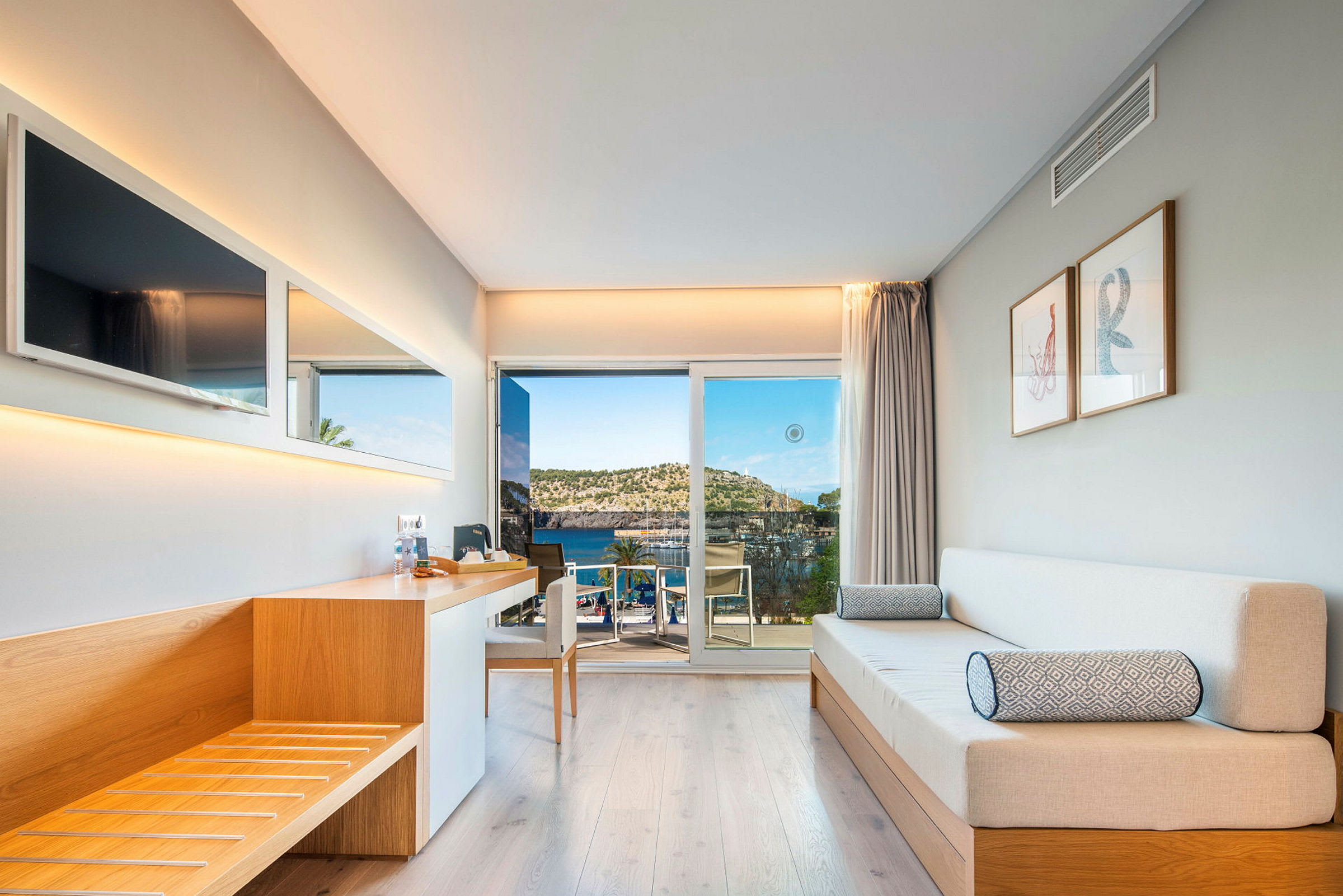 Et moderne hotelværelse med træinteriør, sofa og udsigt over havet gennem en glasdør. (AI-genereret tekst)