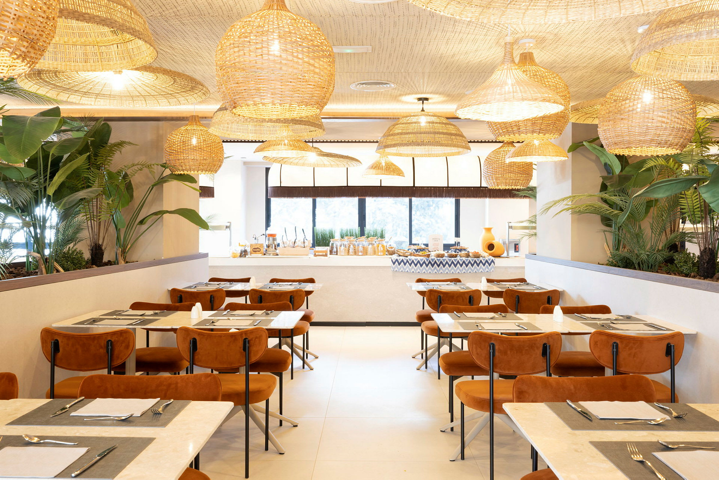 En elegant restaurant med moderne møbler, store vinduer, planter og hængende kurvelamper i loftet. (AI-genereret tekst)