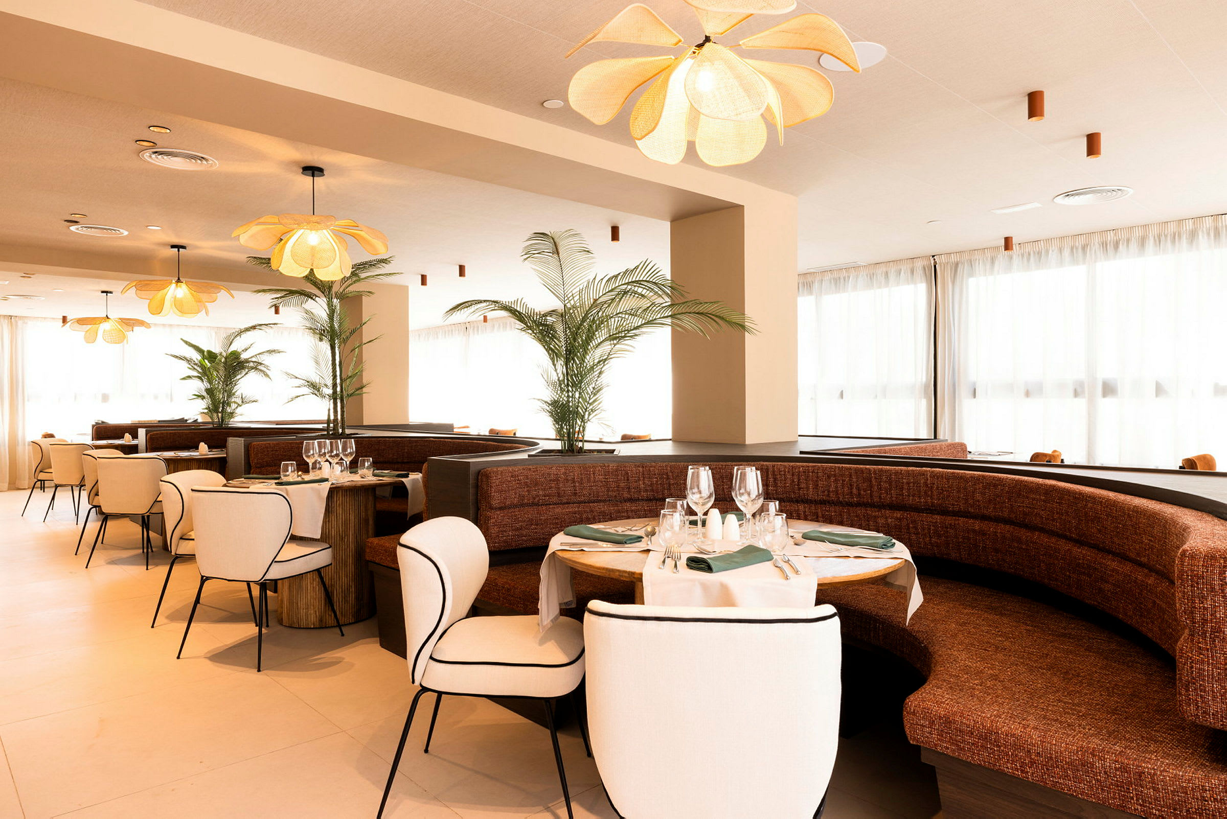 Restaurant med elegant indretning, bestående af runde borde med duge og vinglas samt komfortable stole og sofaer. (AI-genereret tekst)