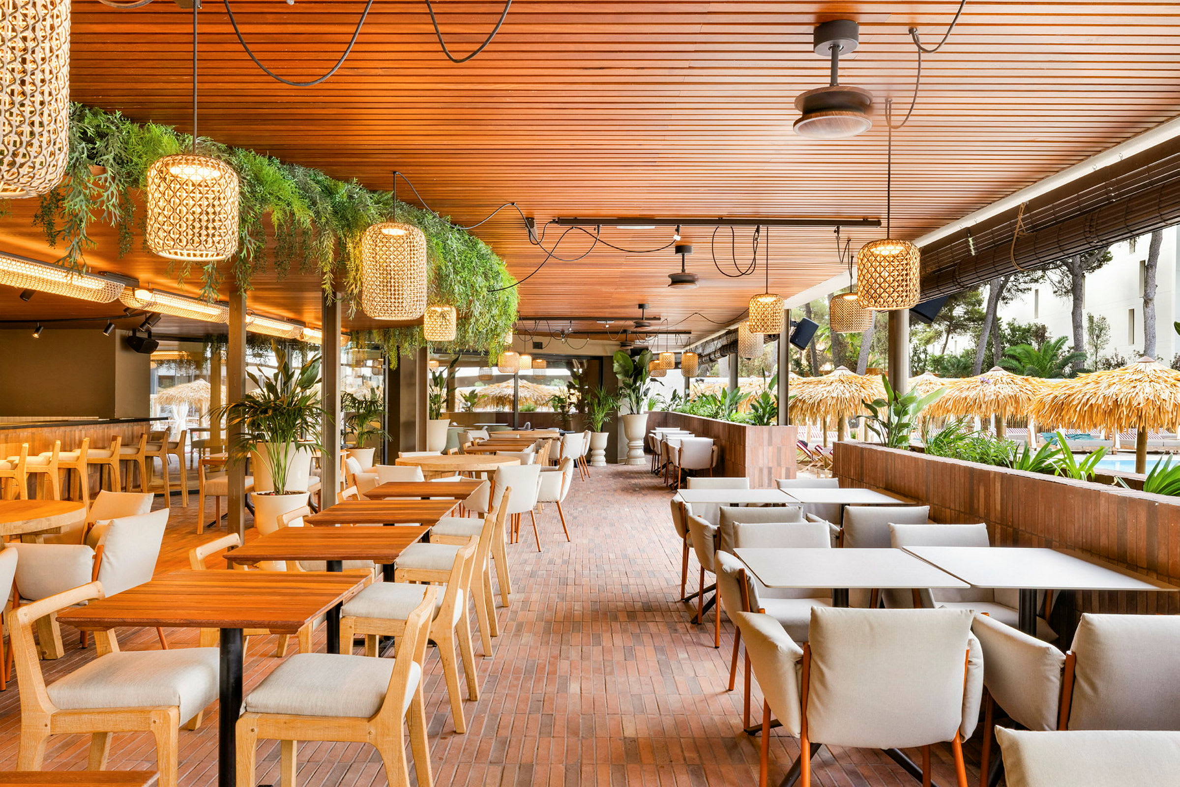 Billede af en lys og moderne udendørsrestaurant med træborde, komfortable stole og dekorative lamper. (AI-genereret tekst)