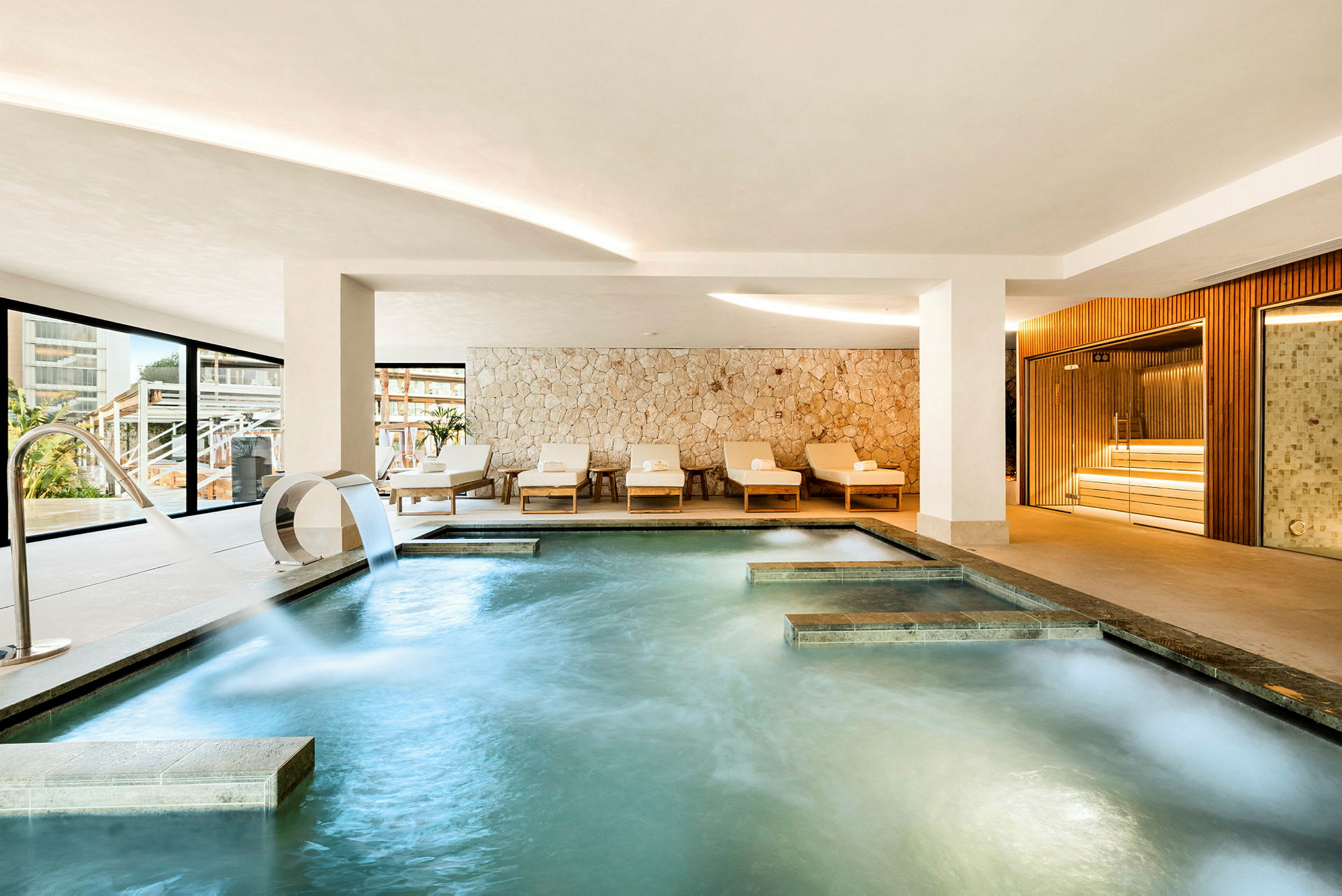 En elegant indendørs pool med moderne møbler og en stenmur i baggrunden. (AI-genereret tekst)