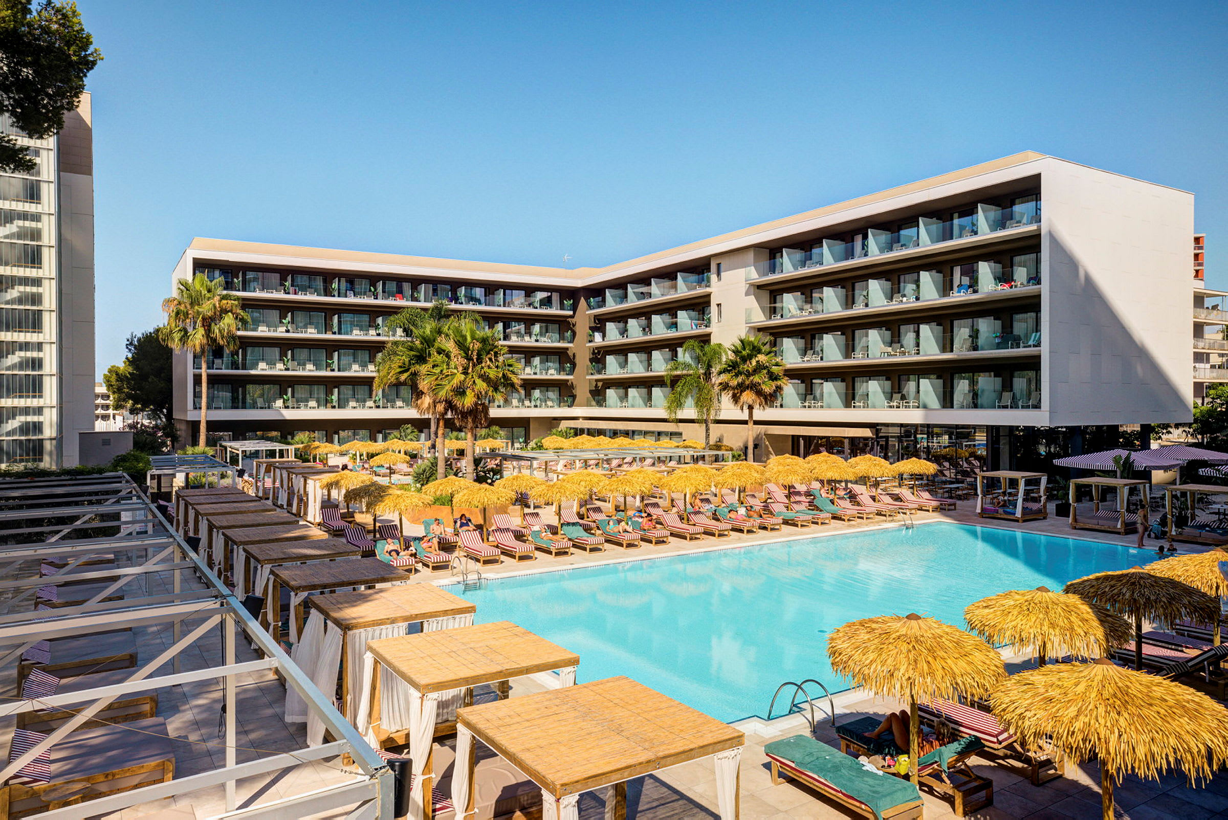 Et moderne hotel med en stor pool, liggestole og parasoller, omgivet af altaner. (AI-genereret tekst)