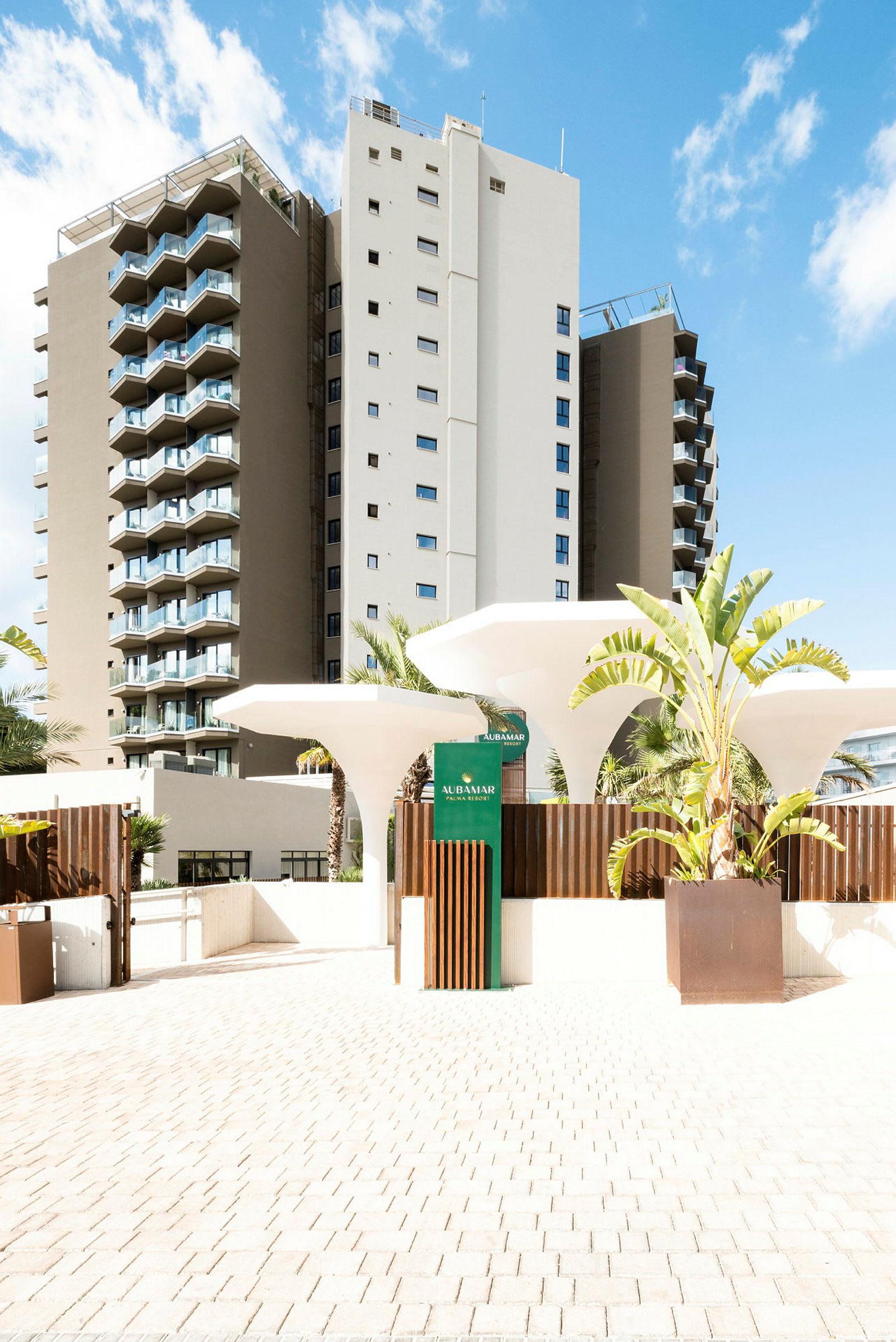 Et hotel i moderne design med hvide og beige facader, flere altaner og frodige planter ved indgangsområdet. (AI-genereret tekst)