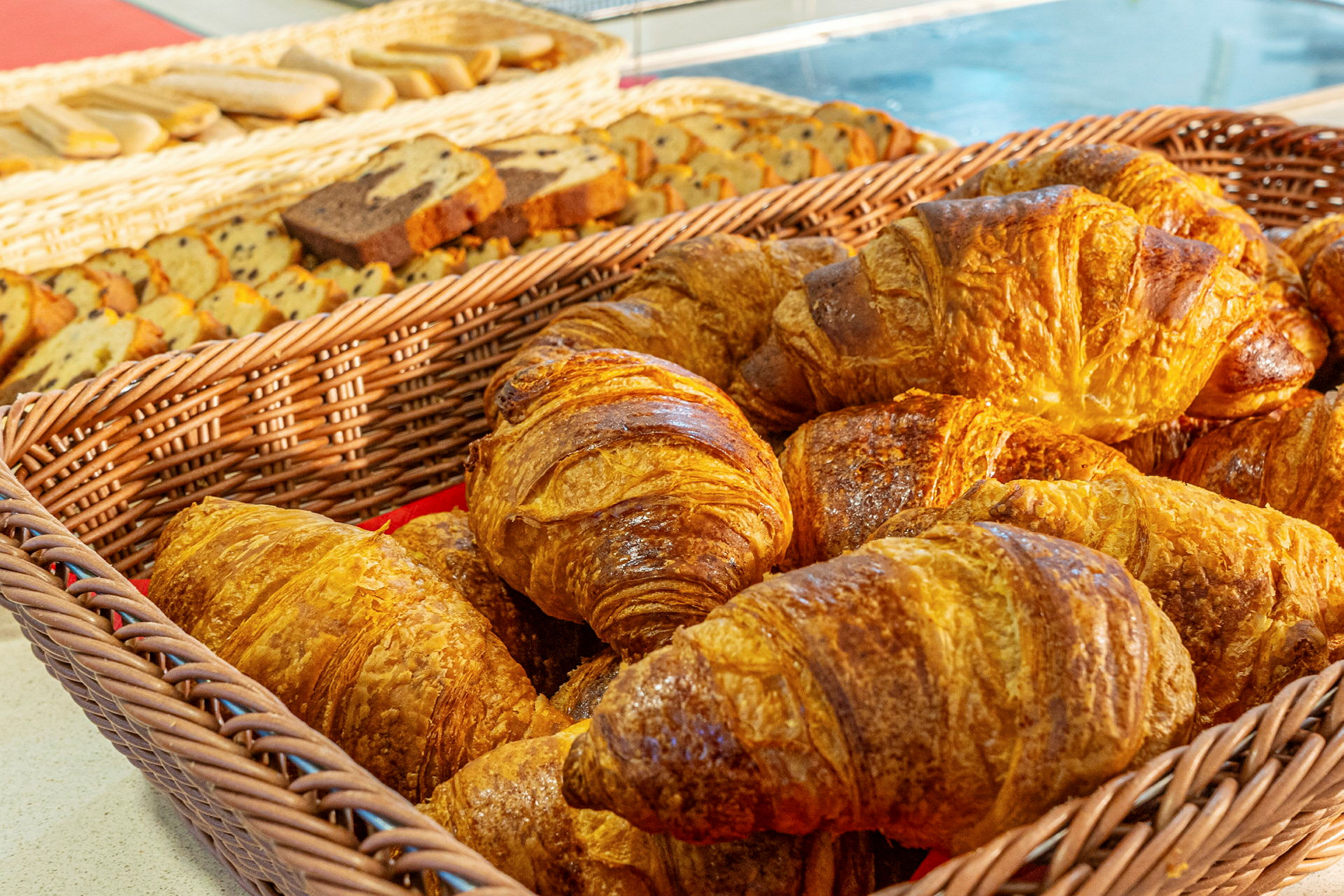 En kurv med croissanter foran en baggrund med forskellige bagværk. (AI-genereret tekst)
