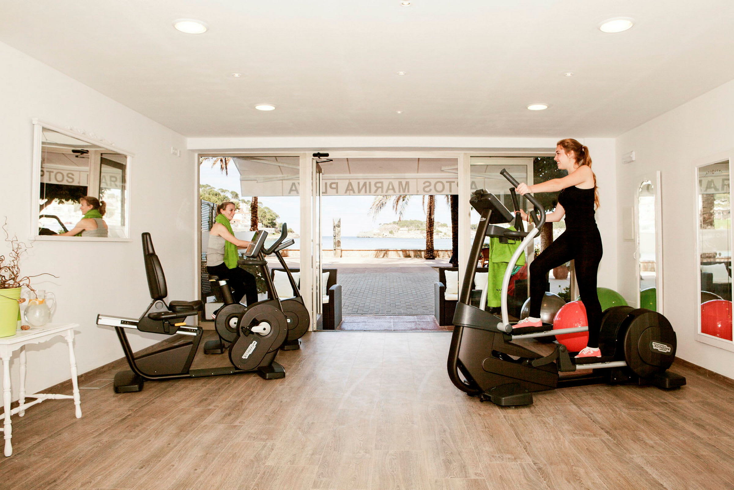 Et fitnesscenter med træningsmaskiner og vinduer mod udendørsområdet. (AI-genereret tekst)
