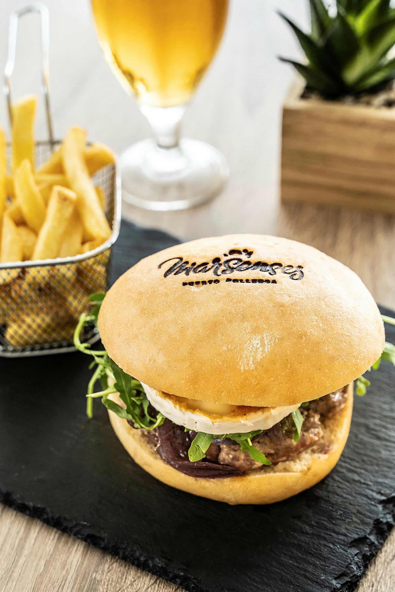 Nærbillede af en burger serveret med pommes frites og et glas øl i baggrunden. (AI-genereret tekst)