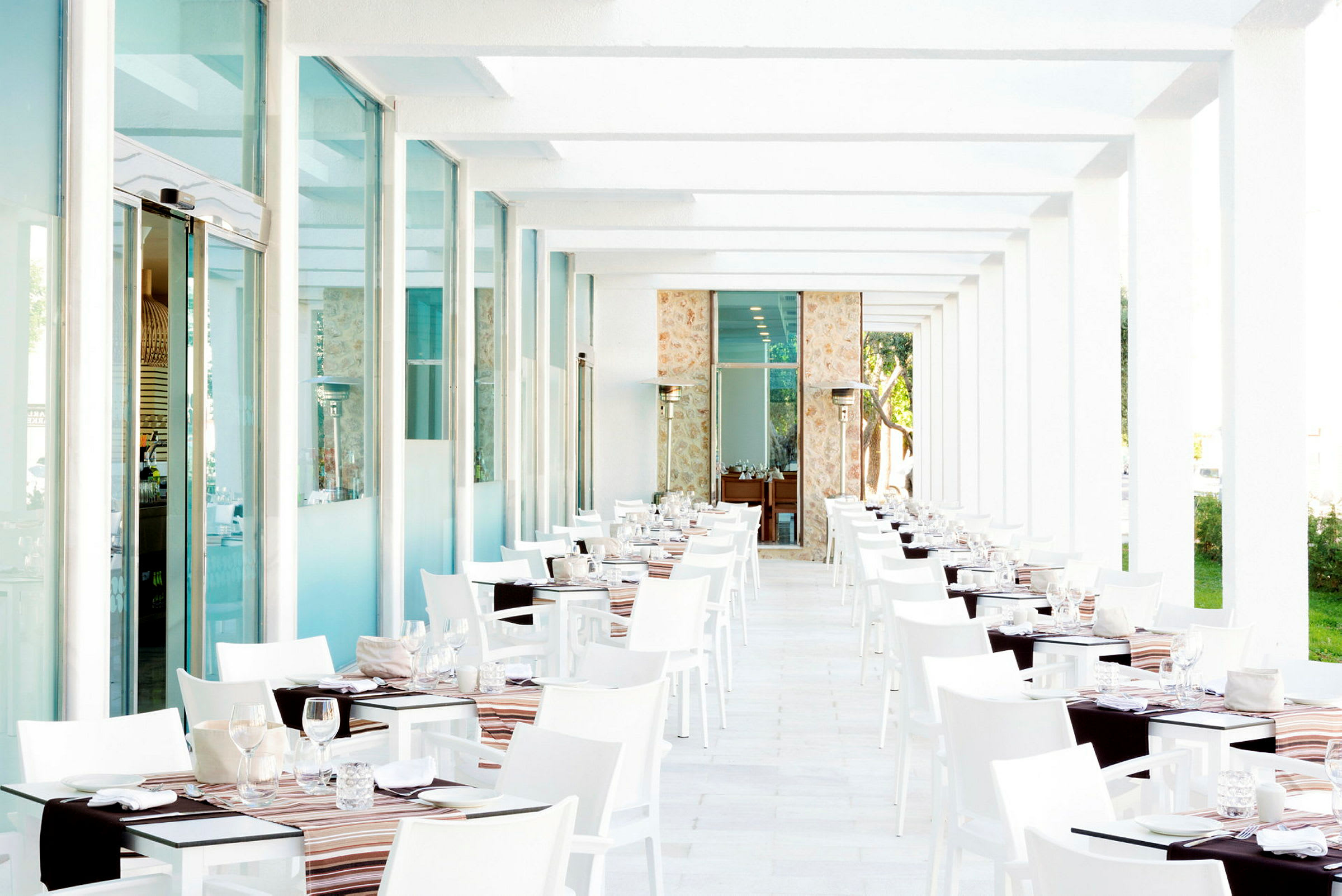 Hvid og moderne restaurantpassage med dækkede borde og glasvinduer. (AI-genereret tekst)