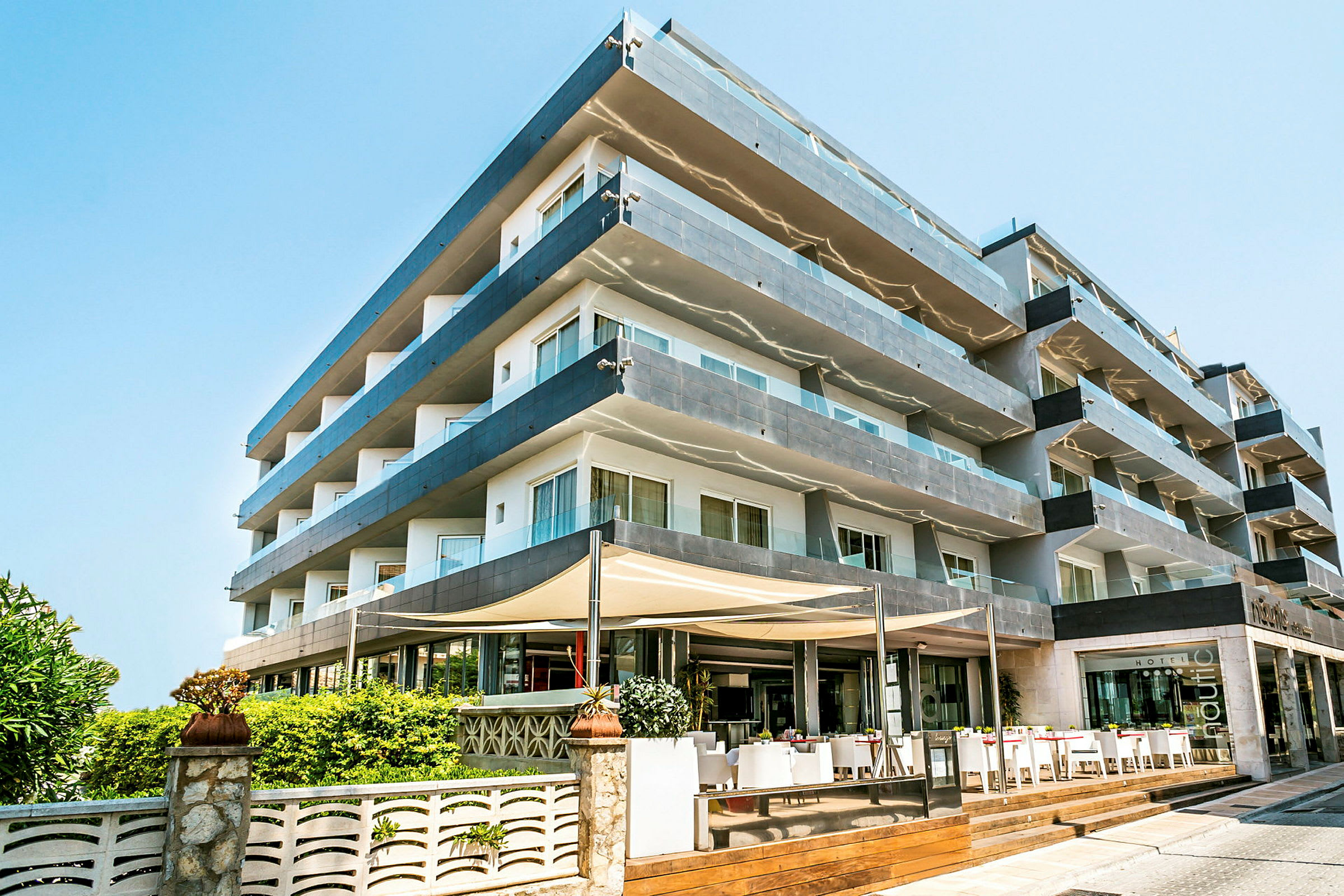 Billede af et fleretagers hotel med glasaltaner og en indgang med udendørsservering. (AI-genereret tekst)