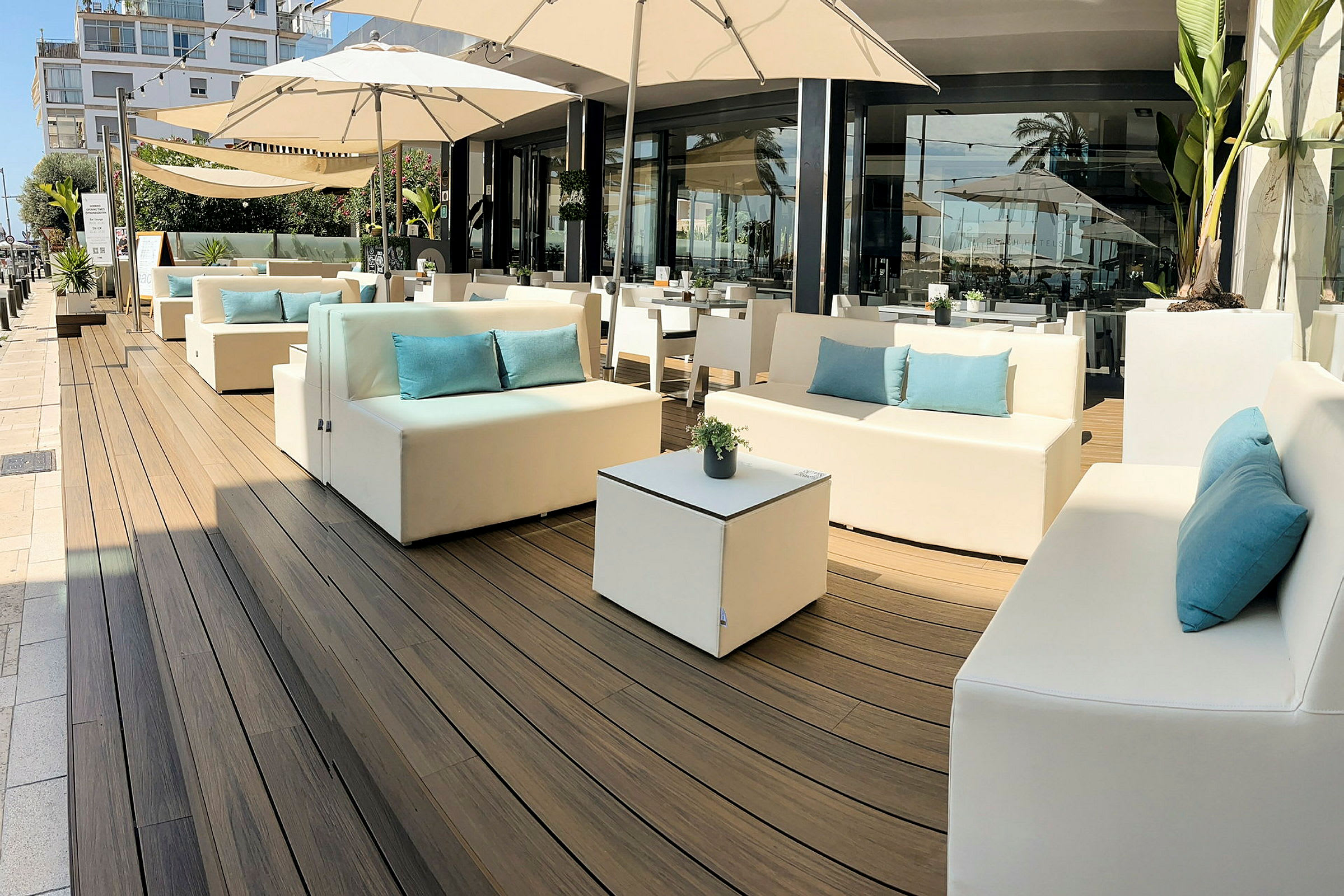Udendørs lounge med hvide sofaer, blå puder og parasoller. (AI-genereret tekst)