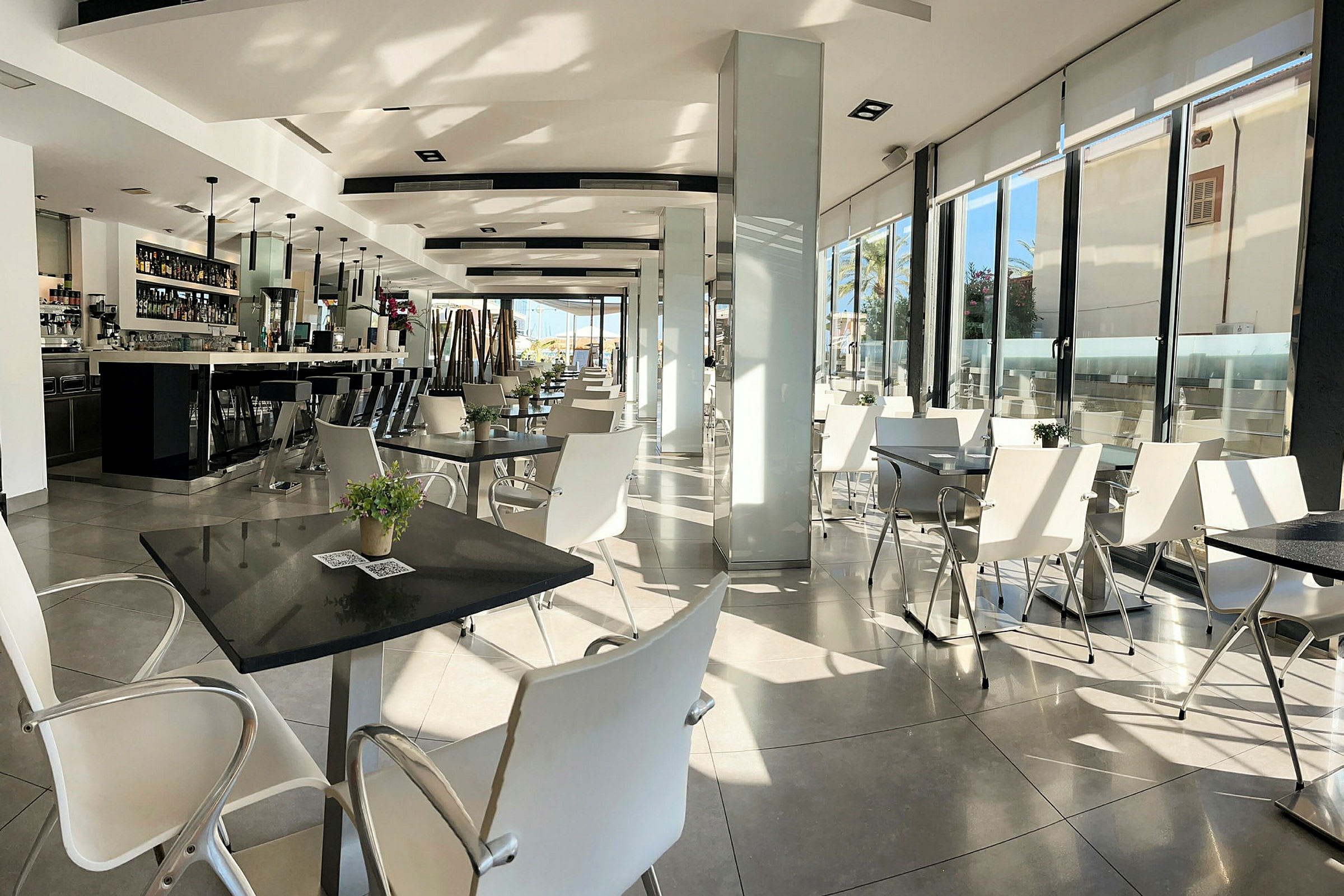 En moderne restaurant med hvide stole og borde, samt en lang bar til venstre. (AI-genereret tekst)