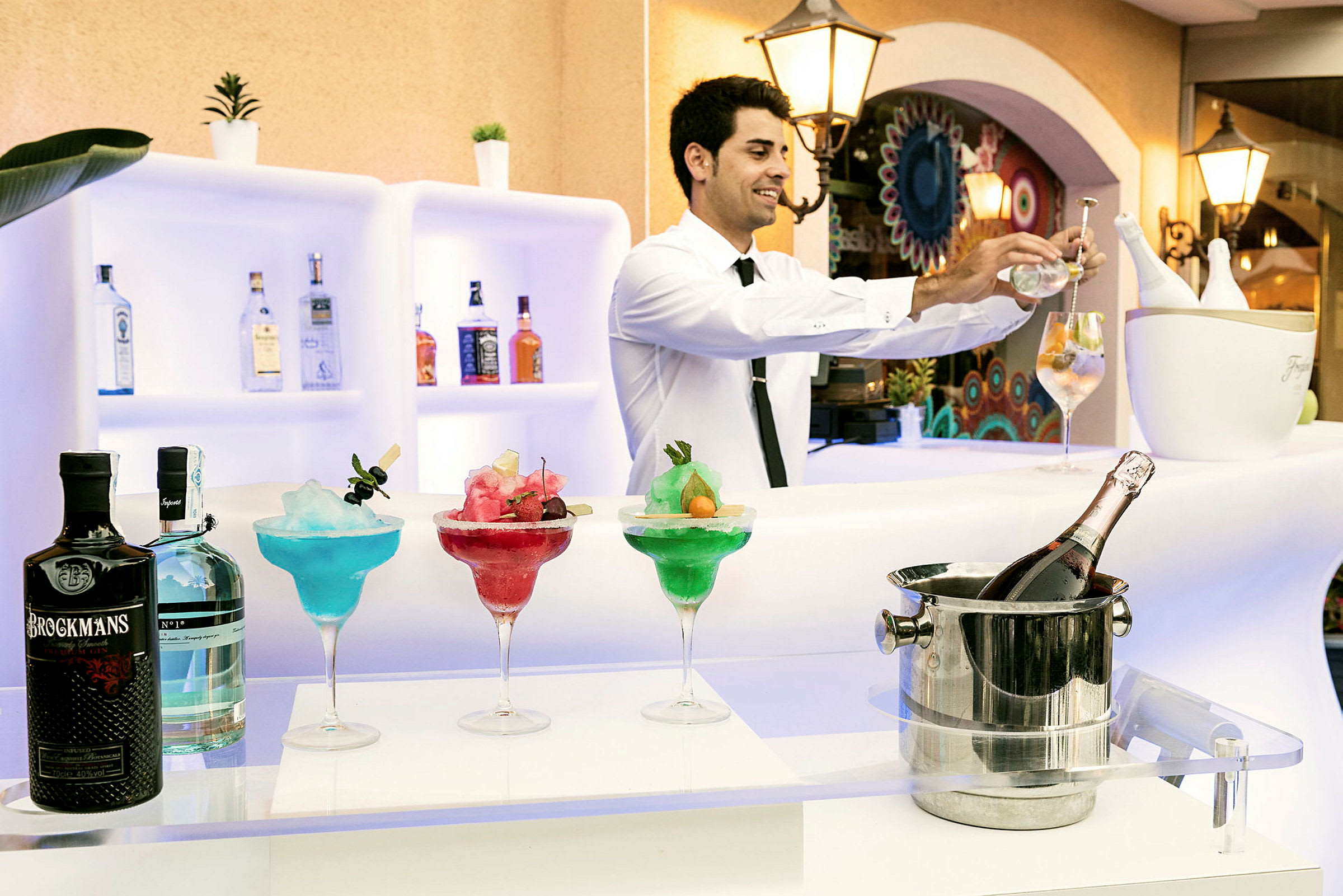 En bardisk med farverige cocktails, flasker og en isspand med en flaske champagne. (AI-genereret tekst)