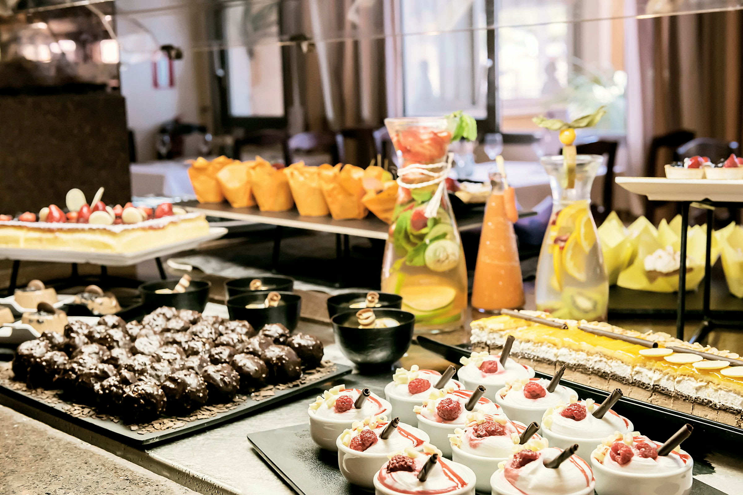 En dessertbuffet med forskellige slags kager, mousse med hindbær, chokolademuffins og en karaffel med citronvand. (AI-genereret tekst)