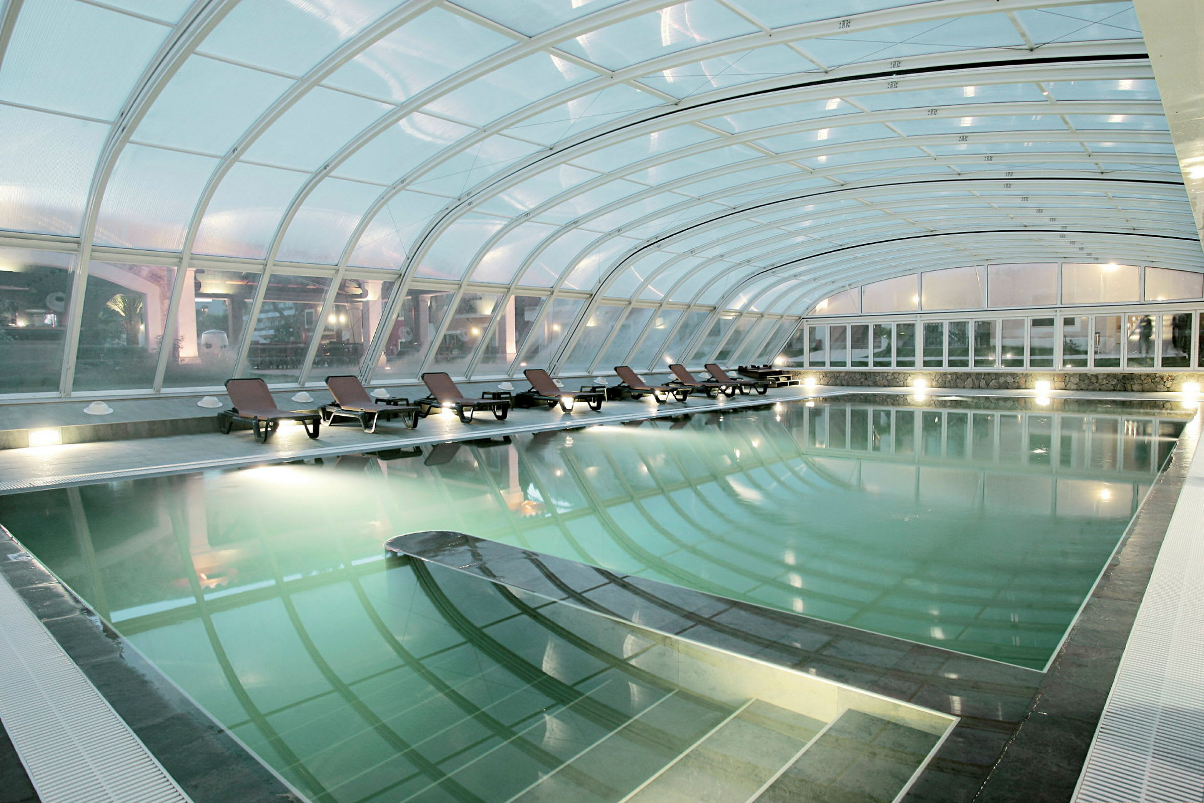 Indendørs swimmingpool med liggestole langs kanten. (AI-genereret tekst)