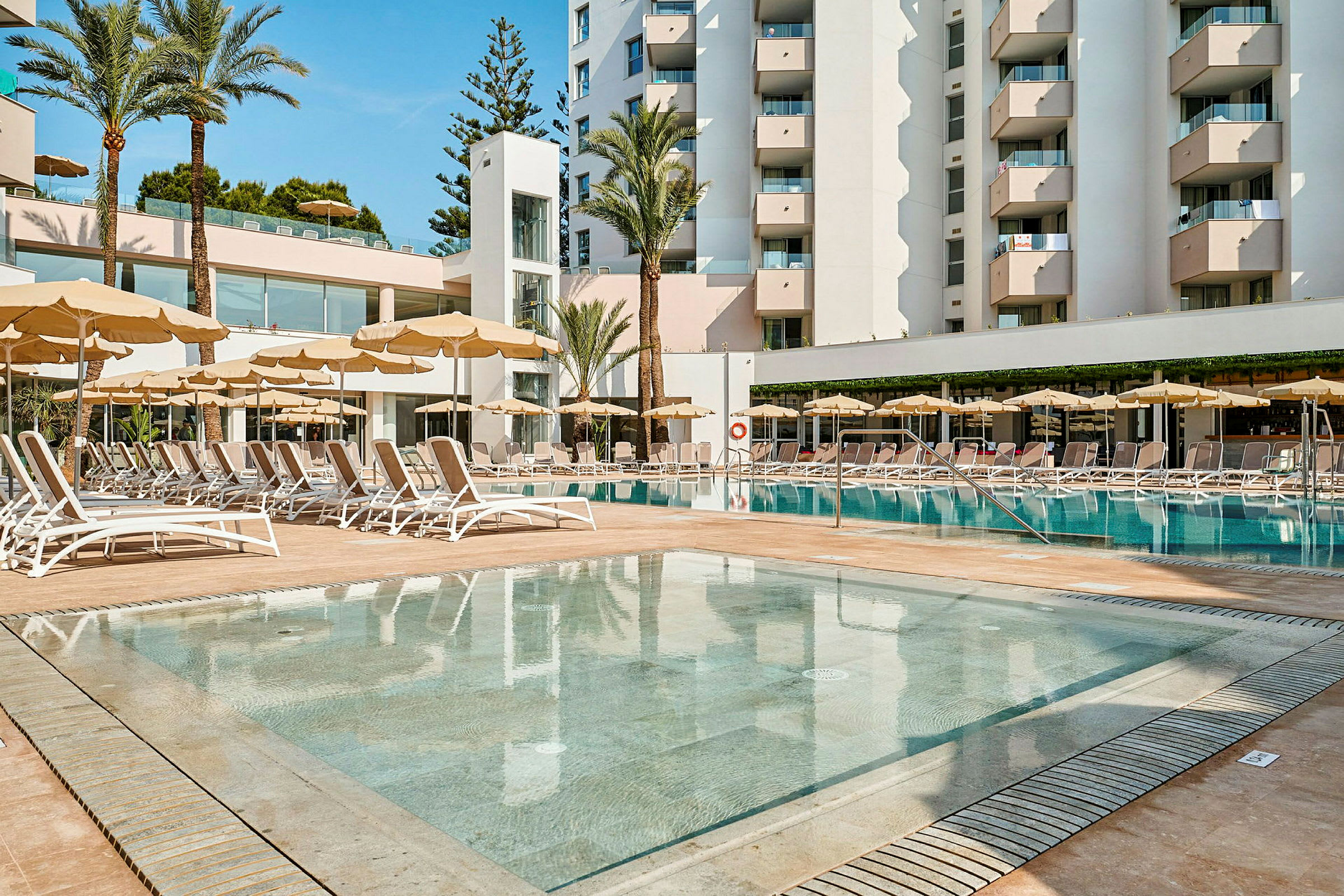 Hotelkompleks med pool og liggestole. (AI-genereret tekst)