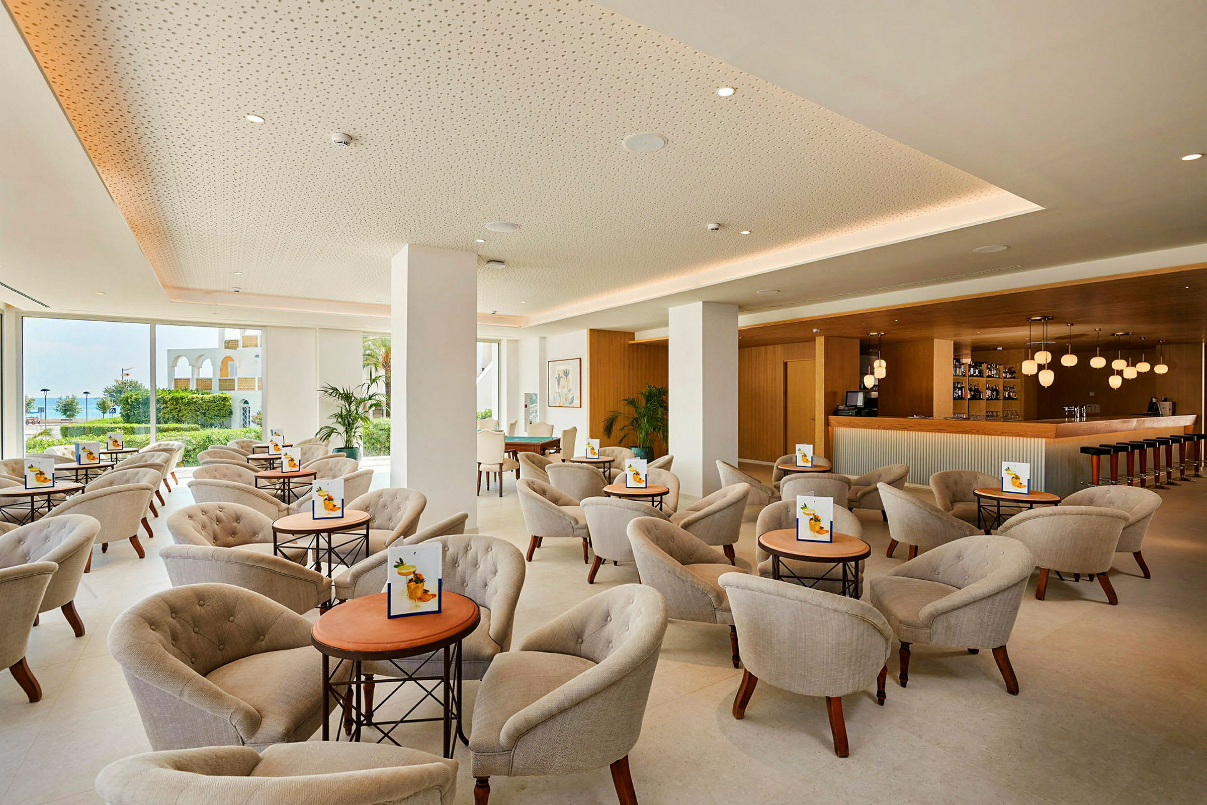 Lys og moderne lounge med stole og små borde samt en bardisk. (AI-genereret tekst)