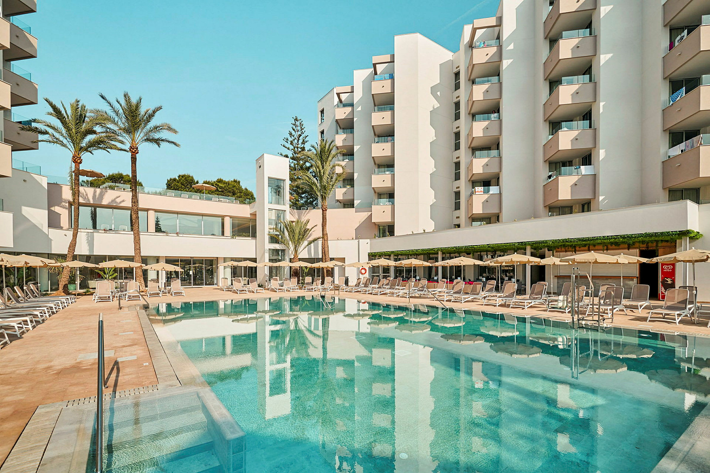 Et hotel med altaner omgiver en pool med liggestole og parasoller. (AI-genereret tekst)