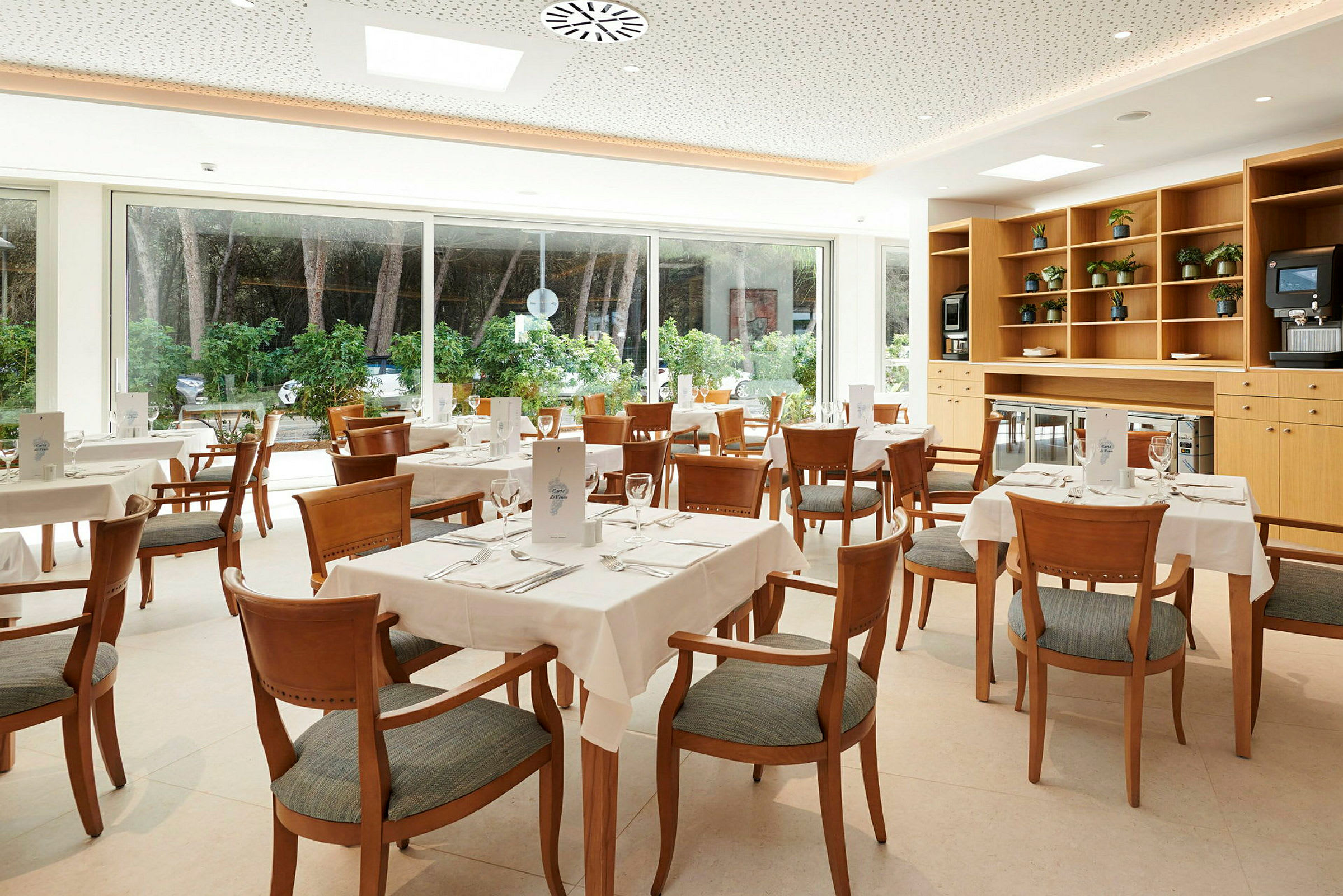 Billede af en lys restaurant med flere dækkede borde og stole. (AI-genereret tekst)