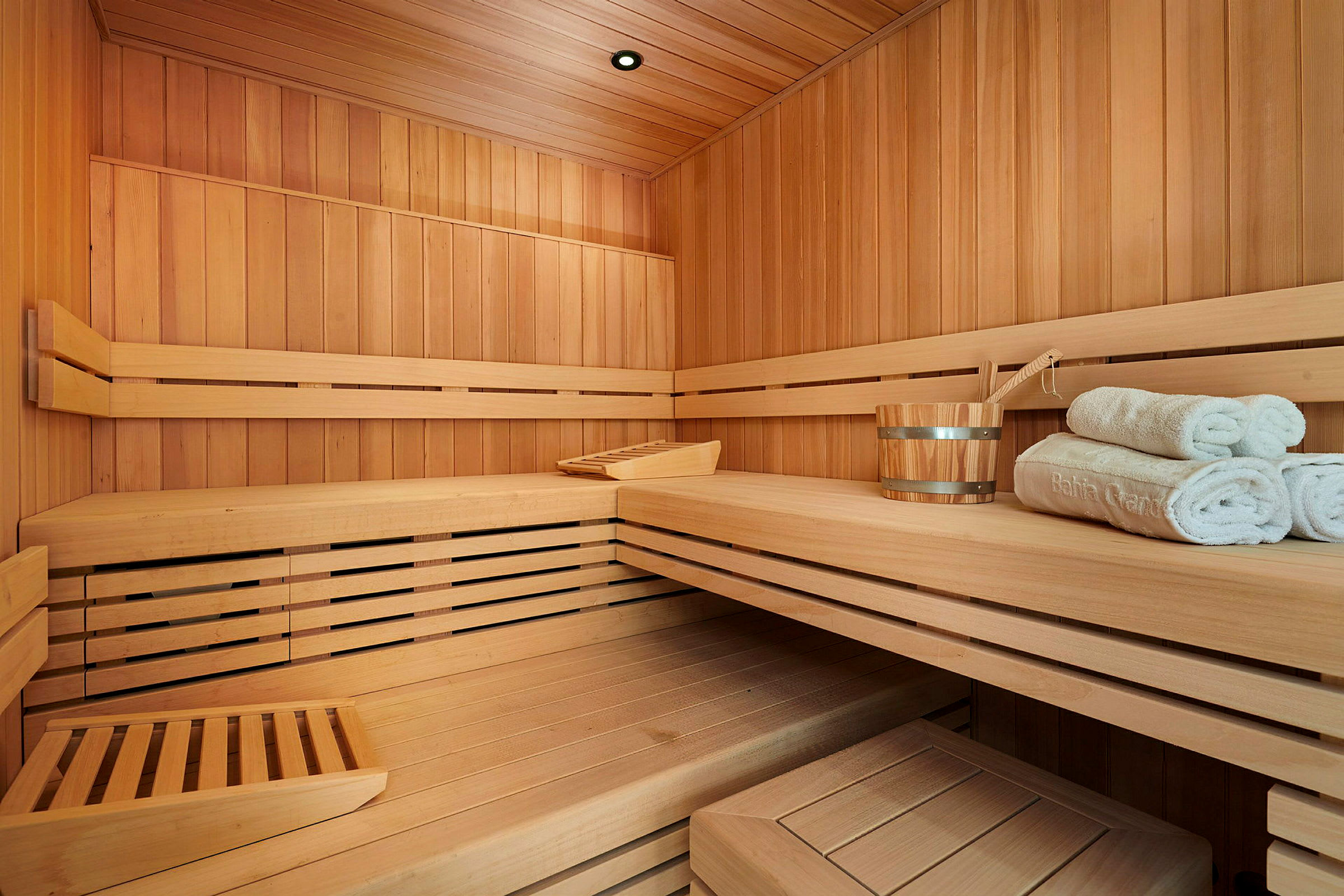 Interiør af en sauna med træpaneler, bænke og en spand med håndklæder. (AI-genereret tekst)