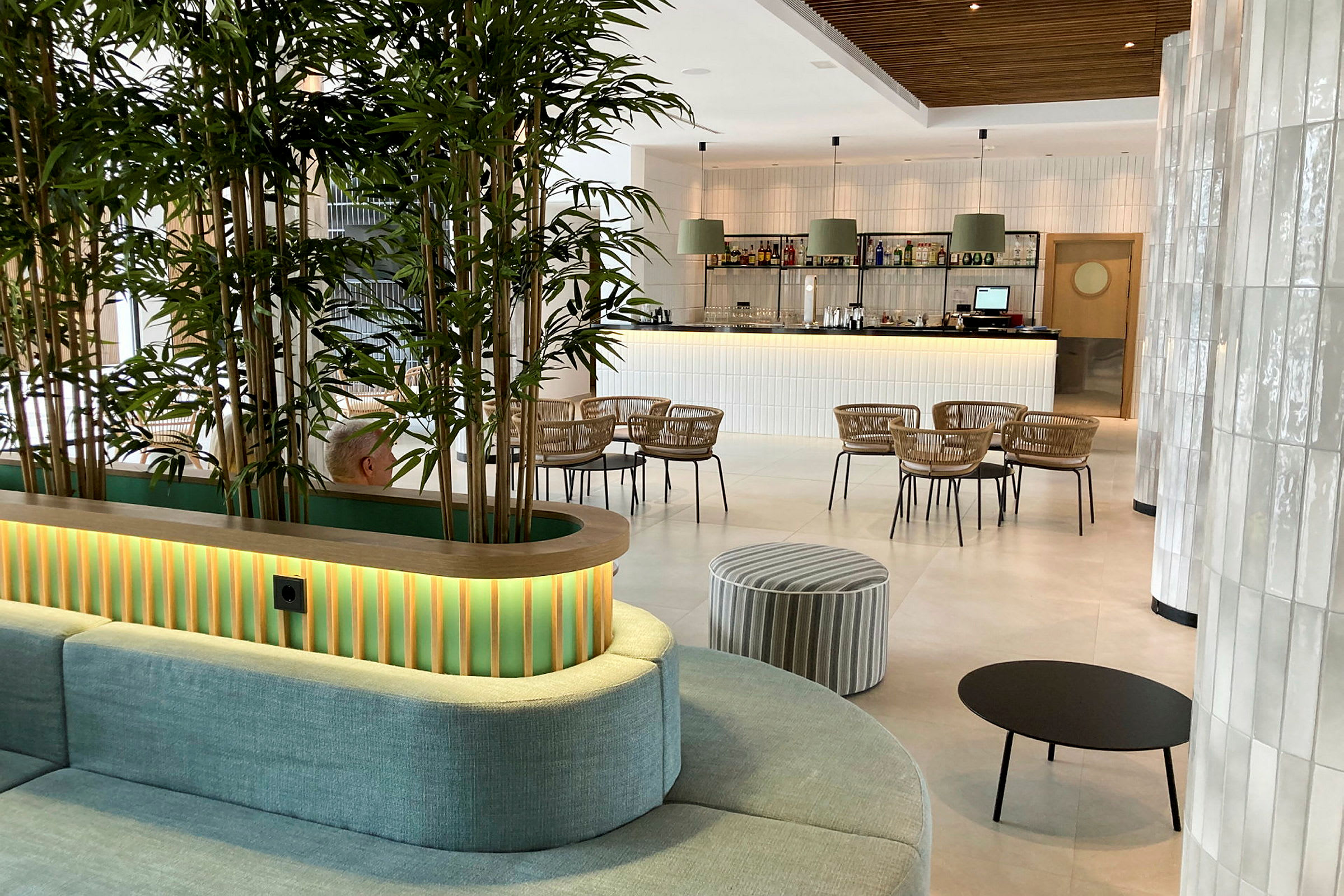 Indretningen i en moderne lounge med grønne planter, siddeområder og en bar i baggrunden. (AI-genereret tekst)