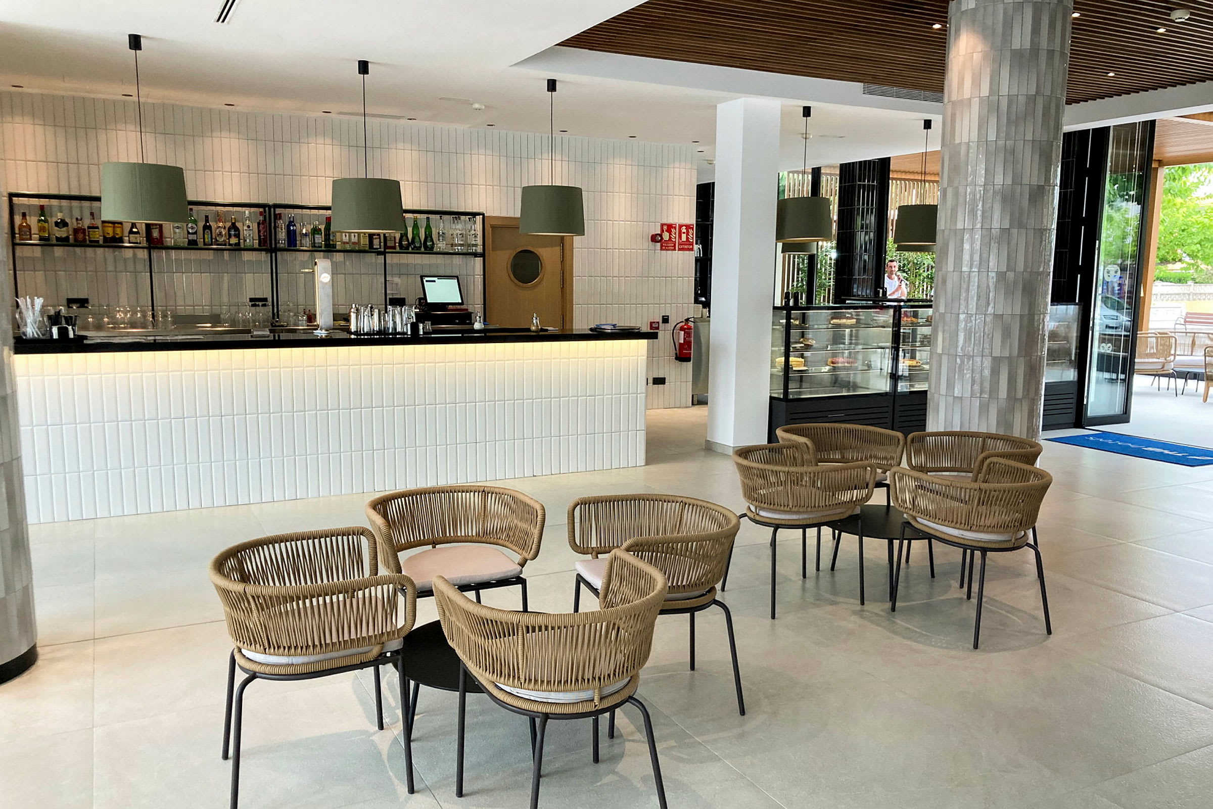 Billede af en moderne lounge med en bar, borde og stole samt en glasmonter med bagværk. (AI-genereret tekst)