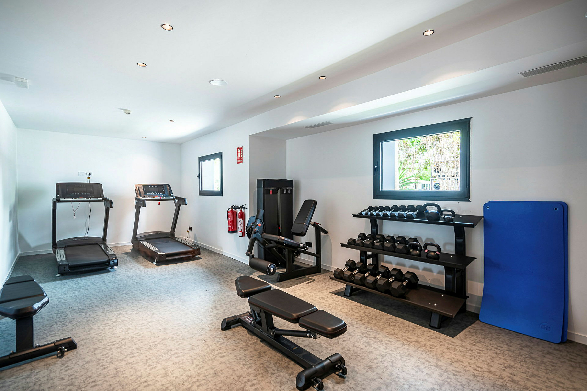 Et fitnesscenter med træningsmaskiner, håndvægte på hylder og løbebånd. (AI-genereret tekst)