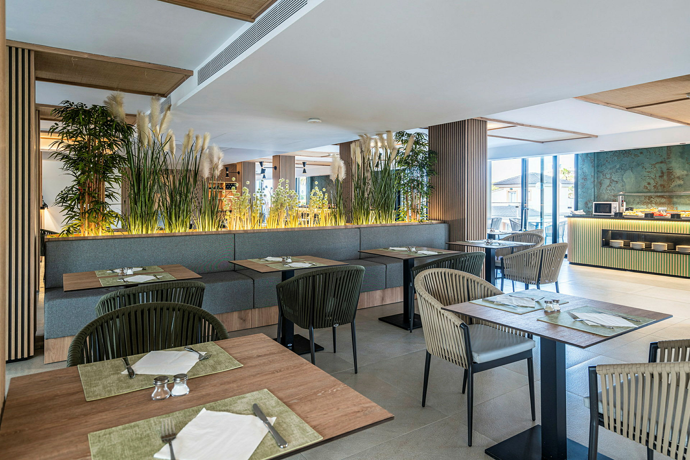 Billede af en moderne restaurant med siddepladser, borde og planter som dekoration. Vinduerne lader naturligt lys strømme ind. (AI-genereret tekst)