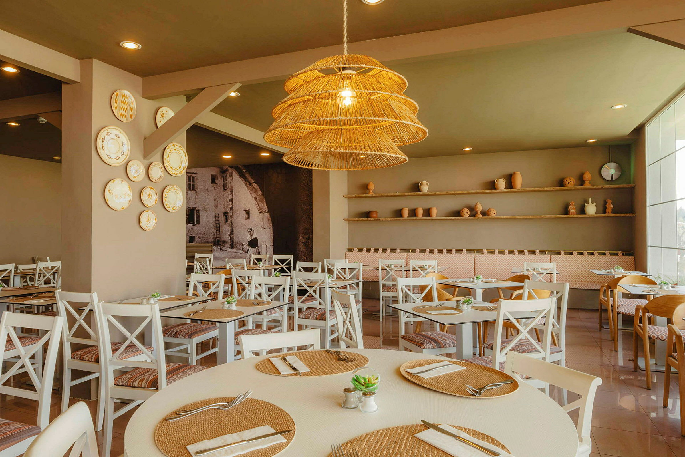 En restaurant med hvide stole, borde med dækning og en dekorativ loftslampe. (AI-genereret tekst)