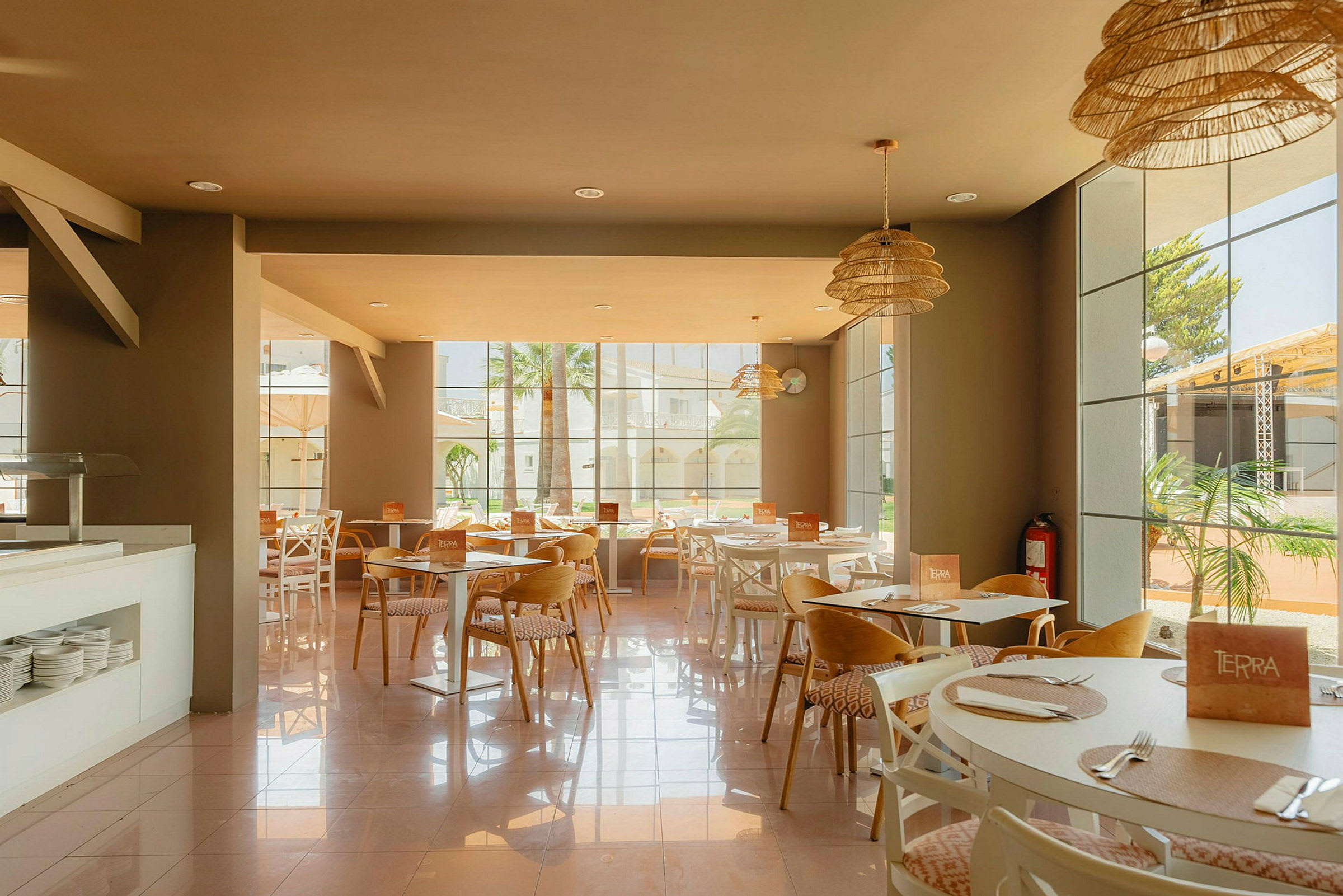 Restaurant med dækkede borde og vinduer der vender ud mod en solrig gårdhave. (AI-genereret tekst)