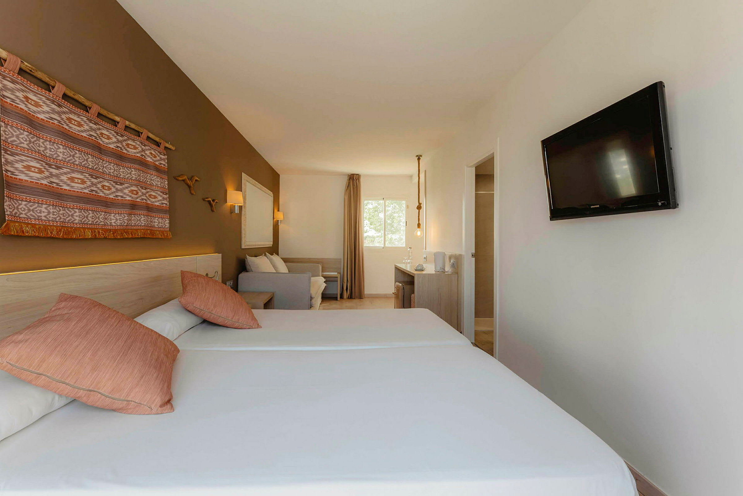 Et hotelværelse med to enkeltsenge, et dekorativt vægophæng, en sofa, et skrivebord og et tv monteret på væggen. (AI-genereret tekst)
