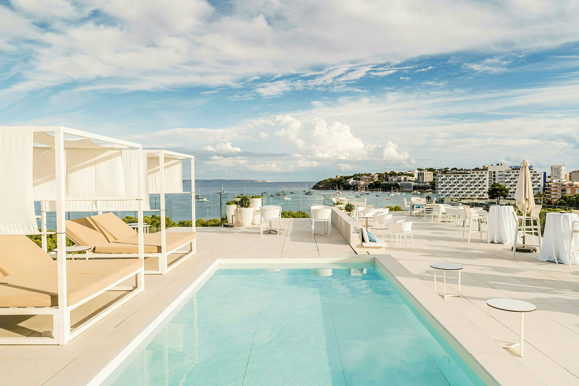En tagterrasse med en pool, liggestole og udsigt over havet og en kystby. (AI-genereret tekst)
