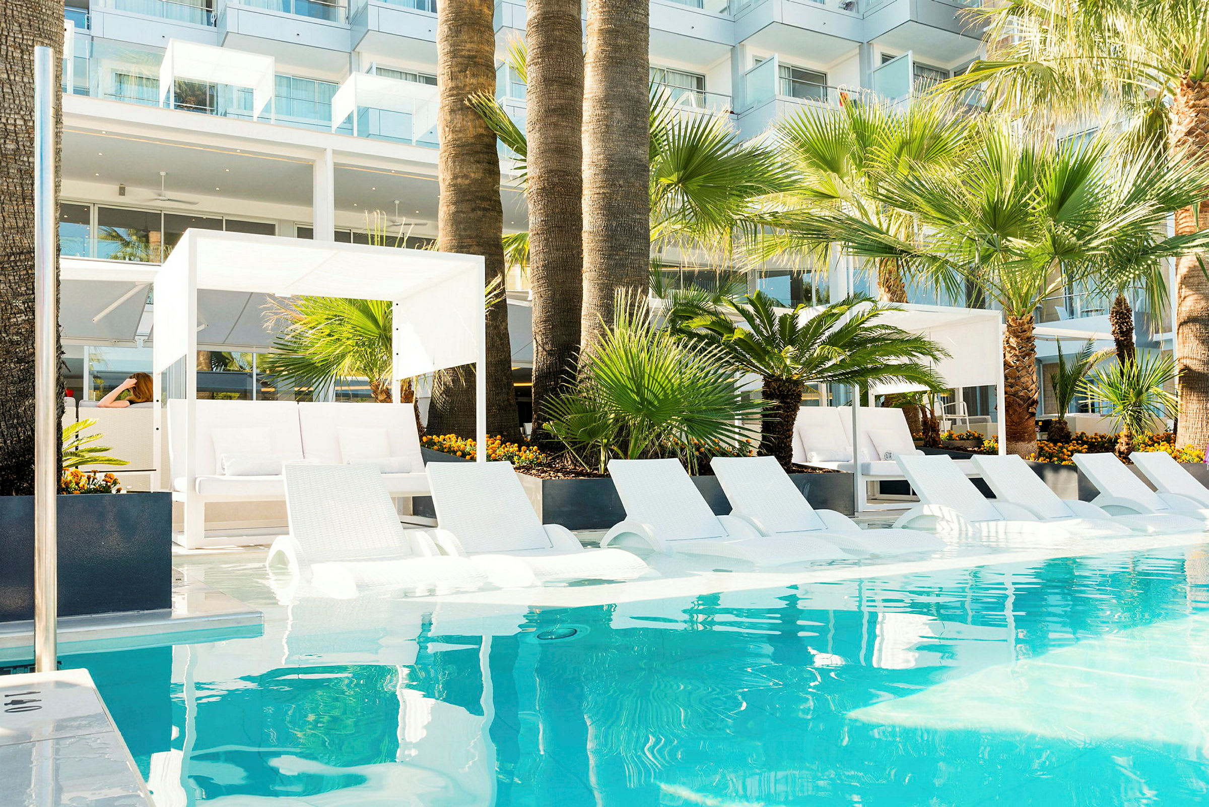 Poolområde med solsenge og palmer ved et moderne hotel. (AI-genereret tekst)