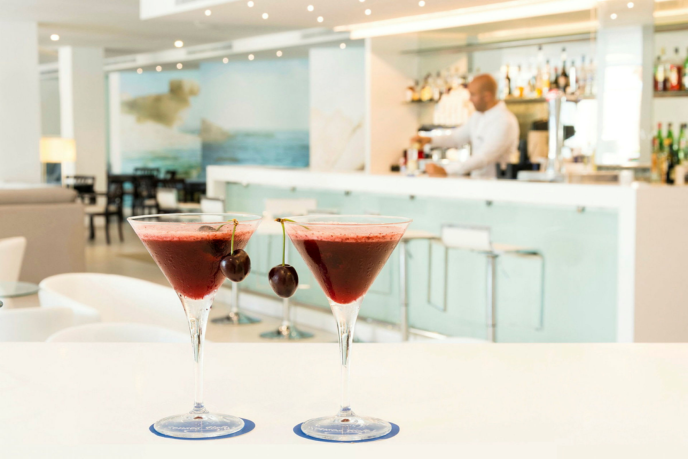 To røde cocktails med kirsebær på toppen står på et bord i en moderne bar. (AI-genereret tekst)