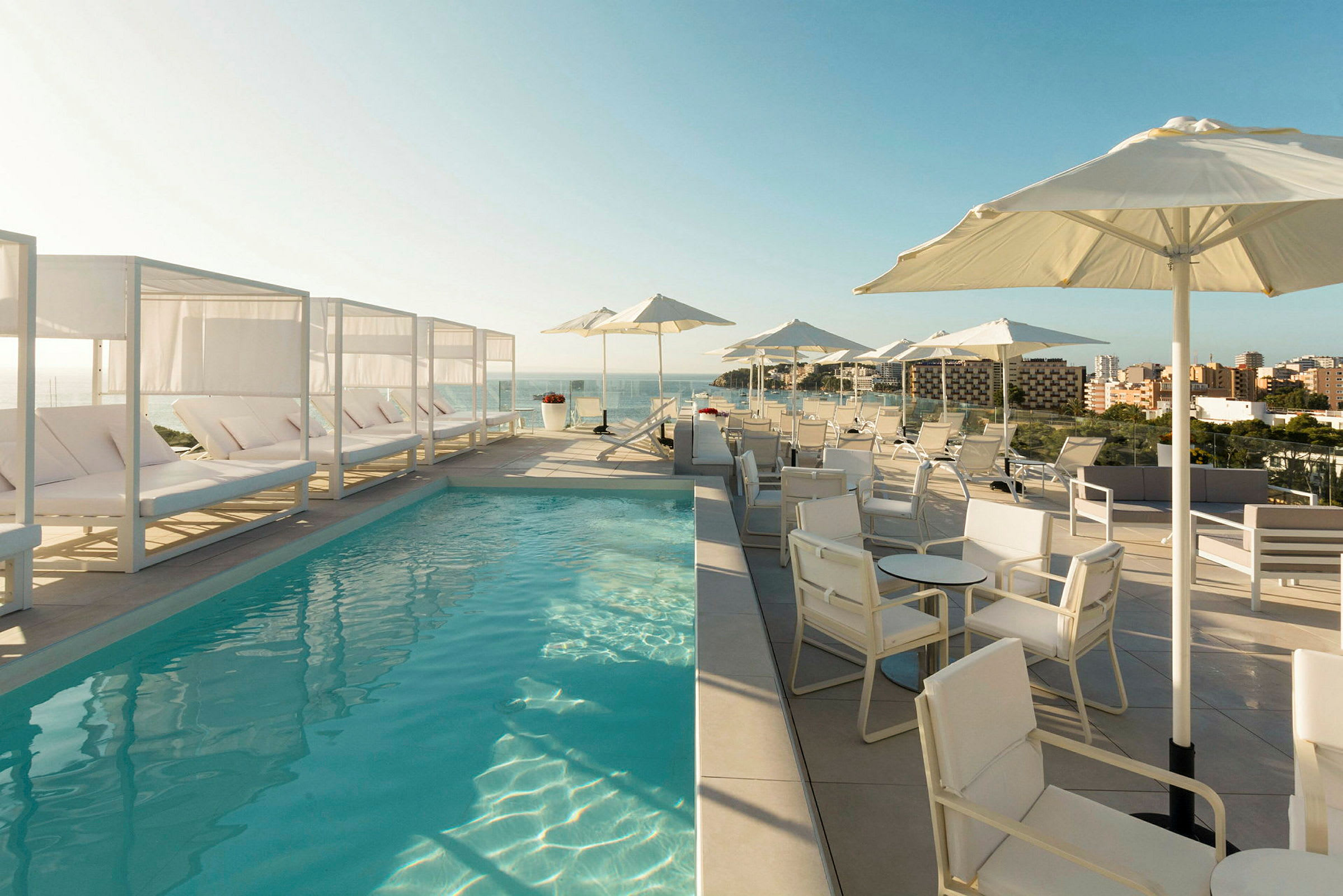 En poolterrasse med liggestole, parasoller og udsigt over byen og havet. (AI-genereret tekst)