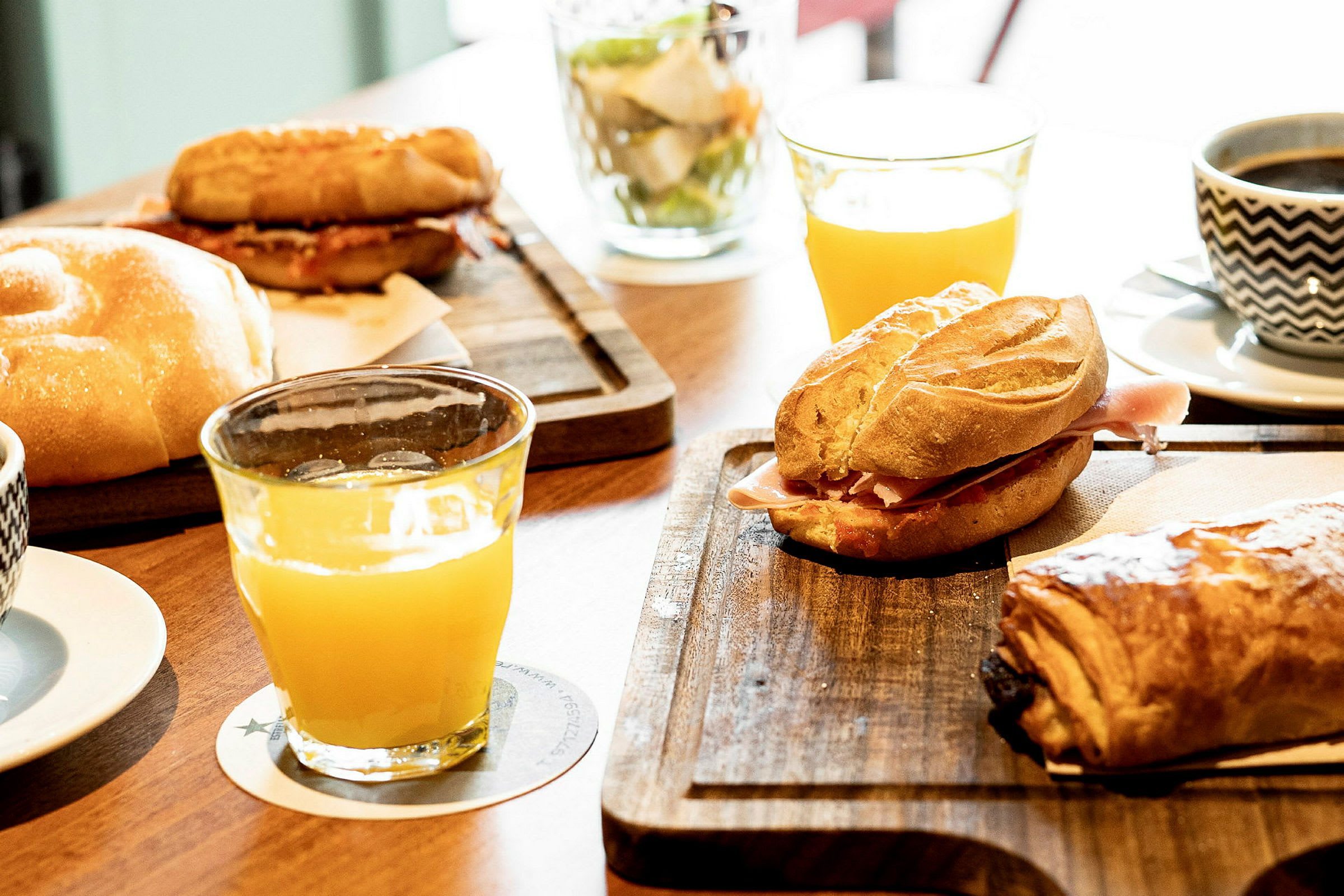 Billedet viser en morgenmadsservering med brød, croissanter, appelsinjuice og kaffe på bordet. (AI-genereret tekst)