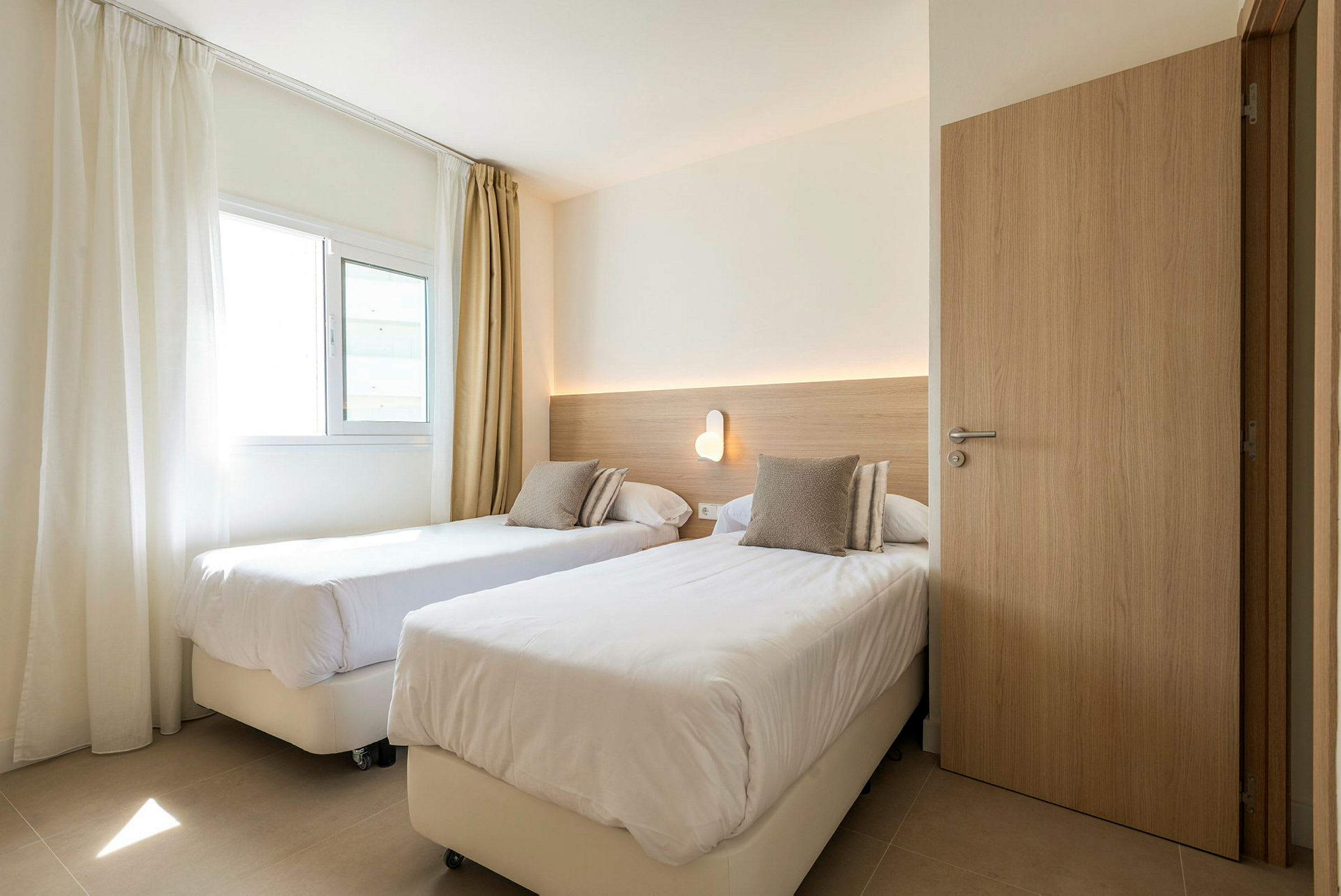 Hotelværelse med to enkeltsenge og en væglampe. (AI-genereret tekst)