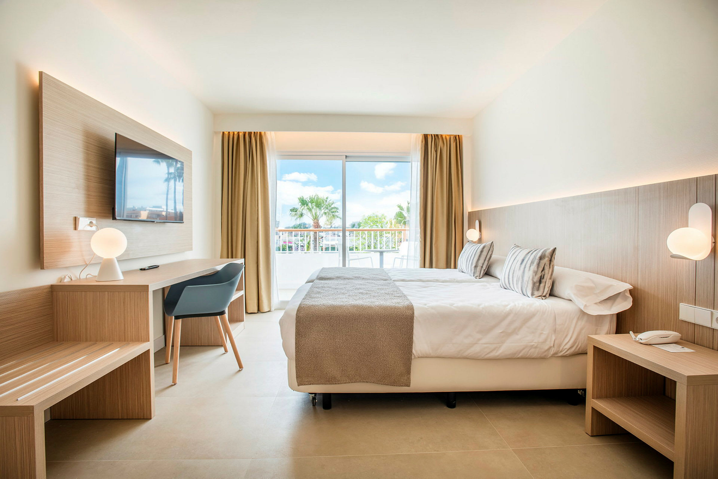 Moderne indrettet hotelværelse med seng, skrivebord og store glasdøre ud til en balkon. (AI-genereret tekst)