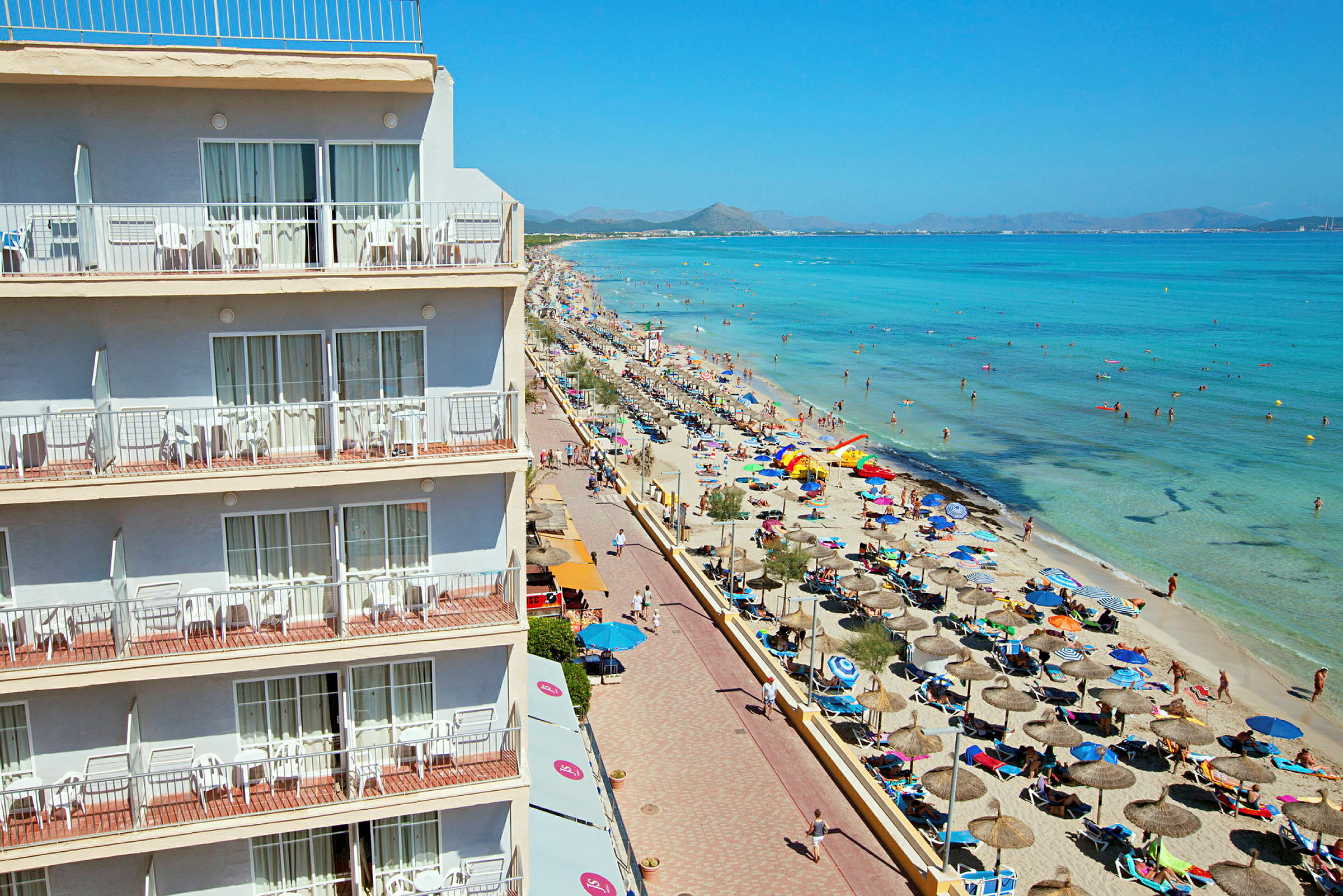 Hotel med altaner ved en livlig strand og klart hav. (AI-genereret tekst)