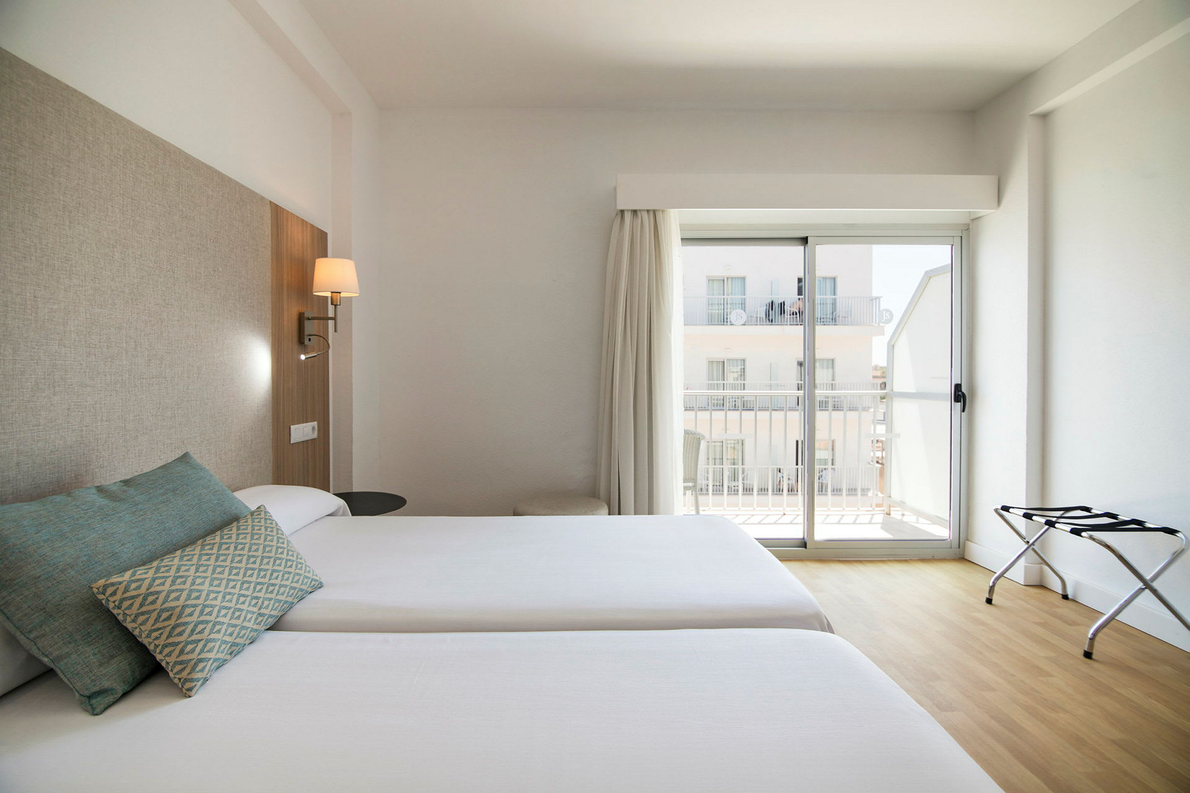 To enkeltsenge på et hotelværelse med lys indretning og et vindue med altan. (AI-genereret tekst)